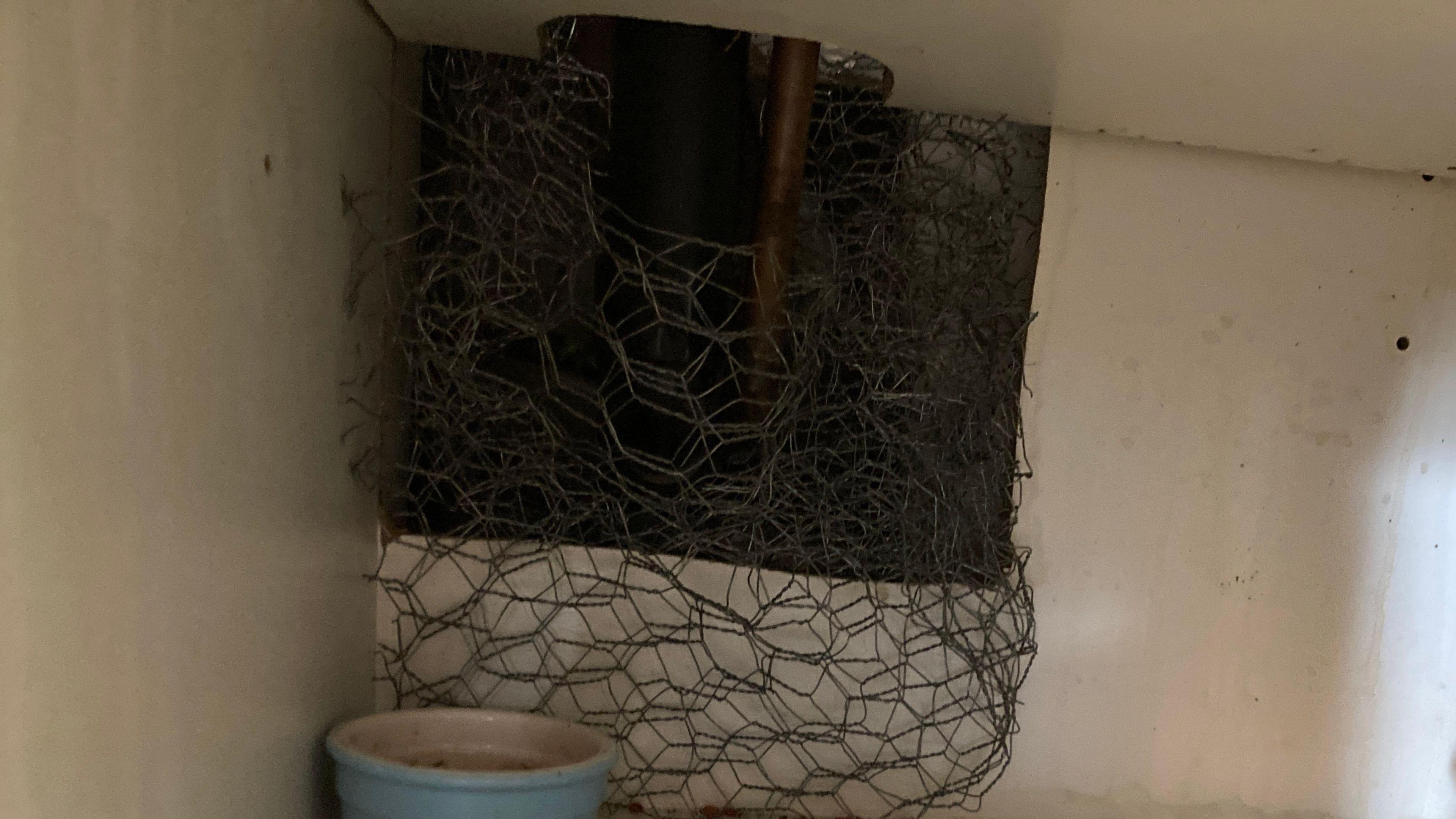 A view of a hole in a cupboard which has been blocked up with chicken wire