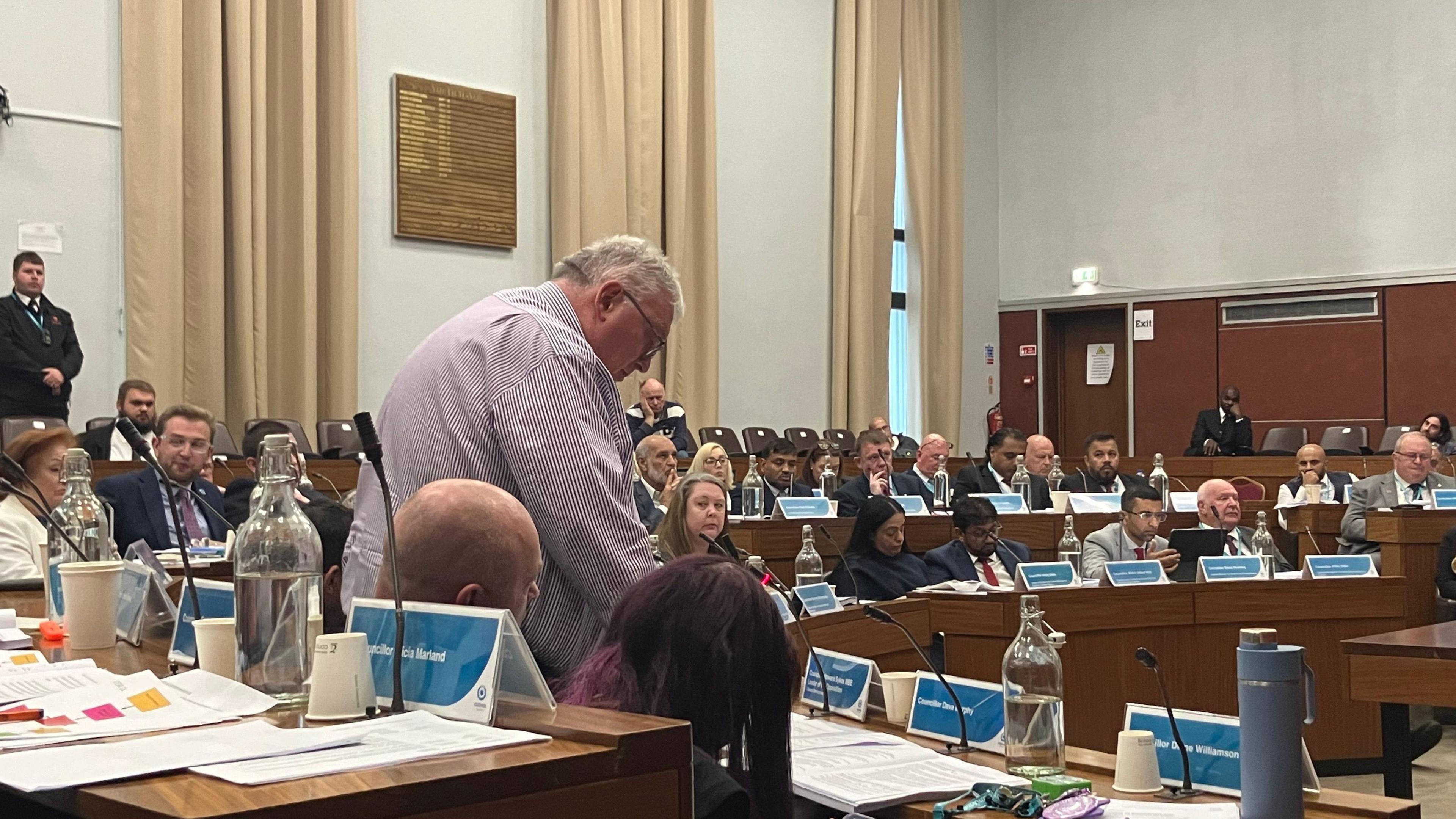 Councillors seated in the Oldham Council chamber, with one councillor standing up to address the meeting