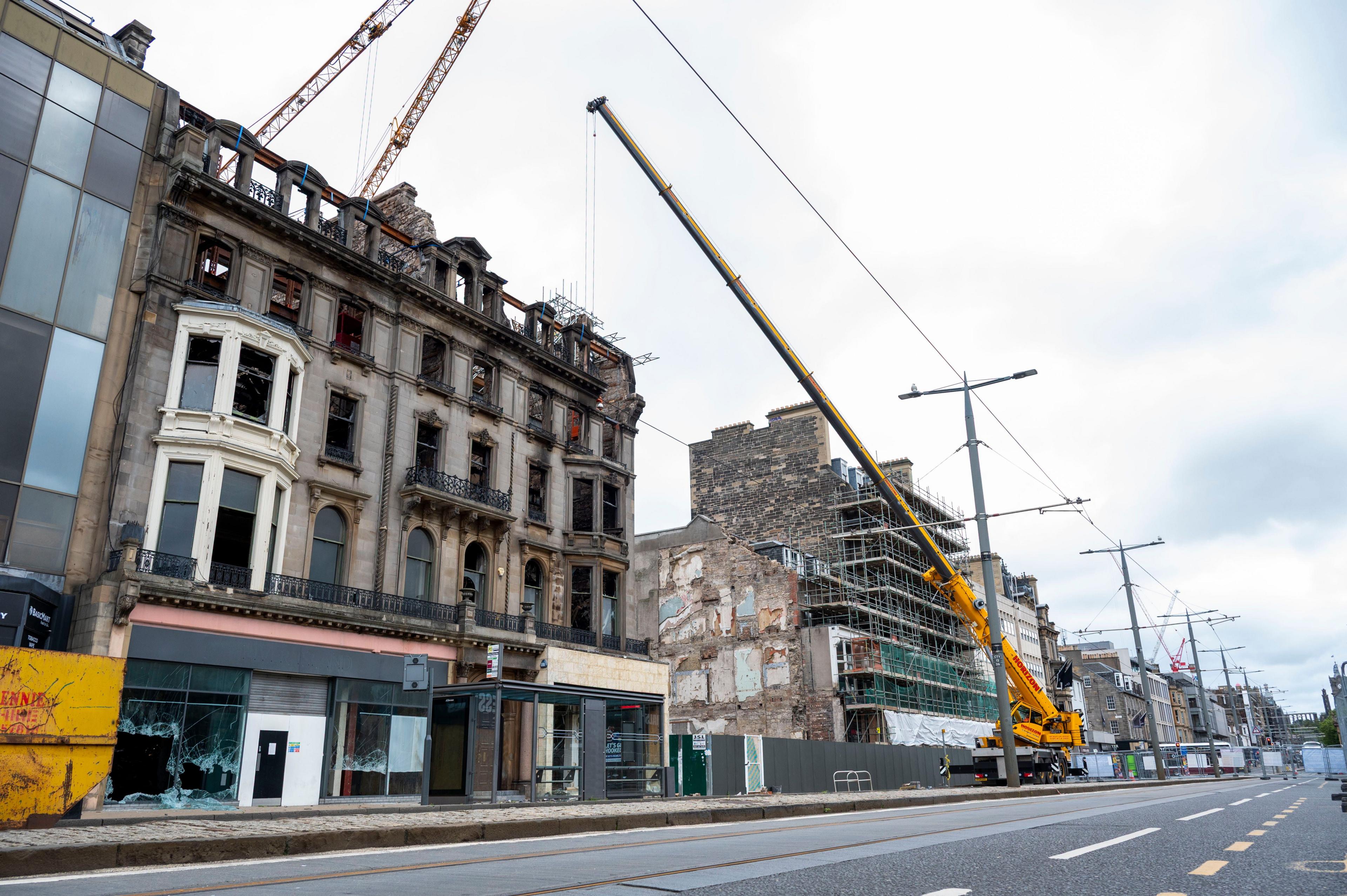 A general view of repair work being carried out on the former Debenhams building in Edinurgh. A large yellow crane is extended over the top of the building, which has been badly damaged and is charred black by a fire.