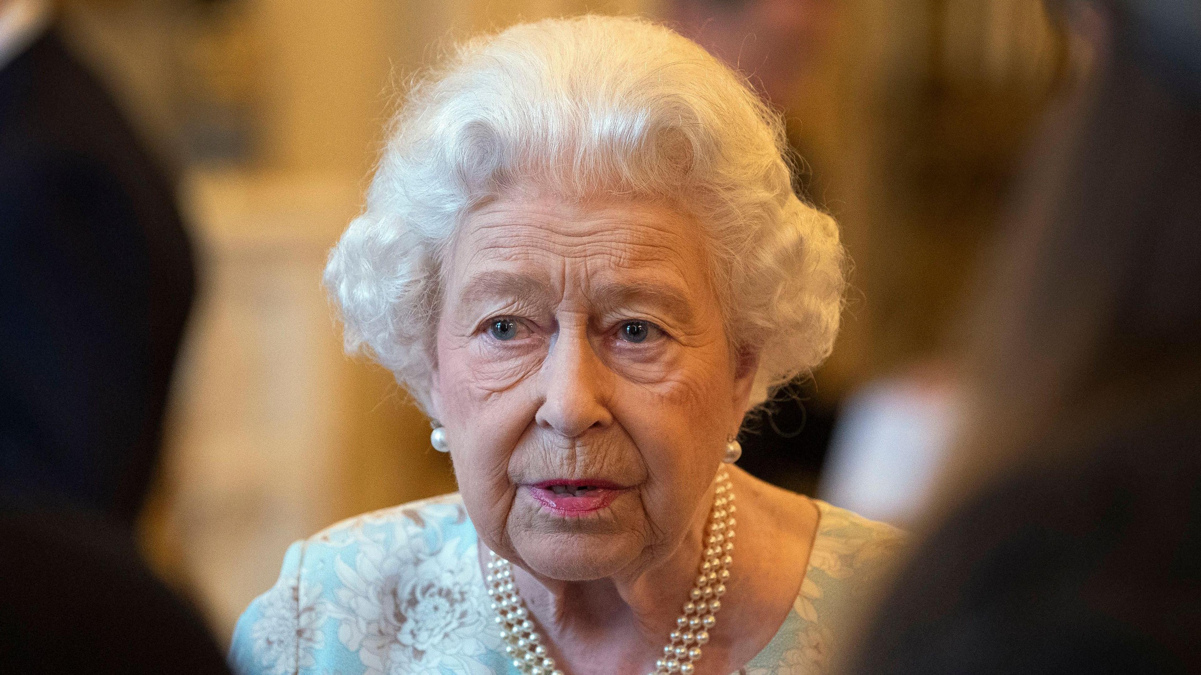 A file photo of Queen Elizabeth at an October 2019 reception in Buckingham Palace, wearing a string of pearls, pearl earrings and a floral dress in pale blue and white with accents of taupe.