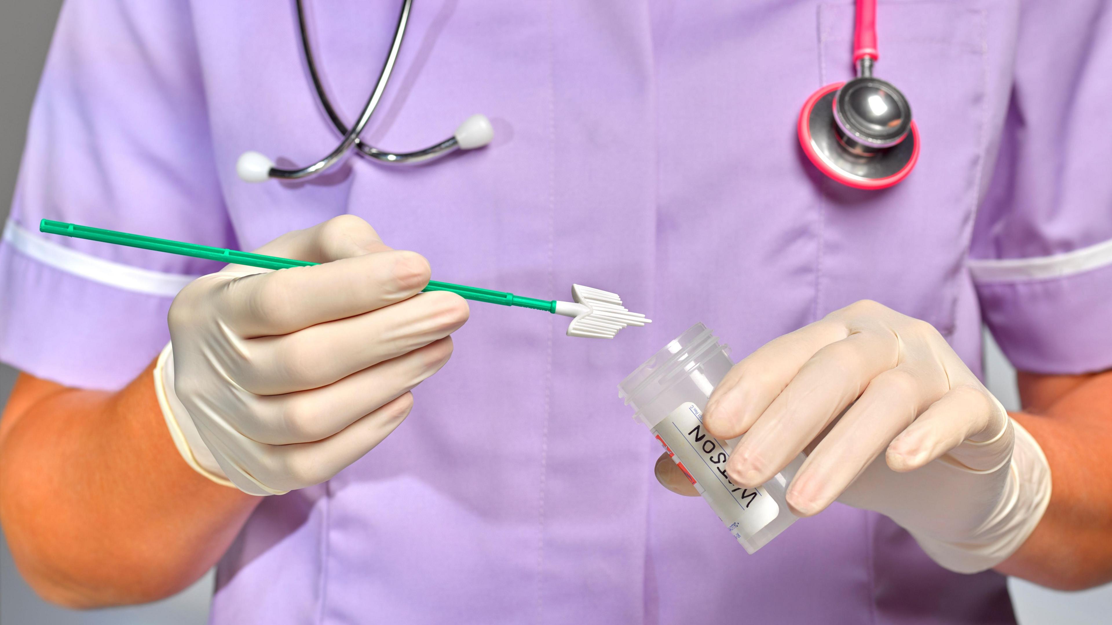 Practice Nurse or doctor doing a smear test.  She is holding a tool with a sample from a smear test and putting it into a tube. A pink stethoscope is around her neck and she's wearing a purple uniform and disposable gloves.