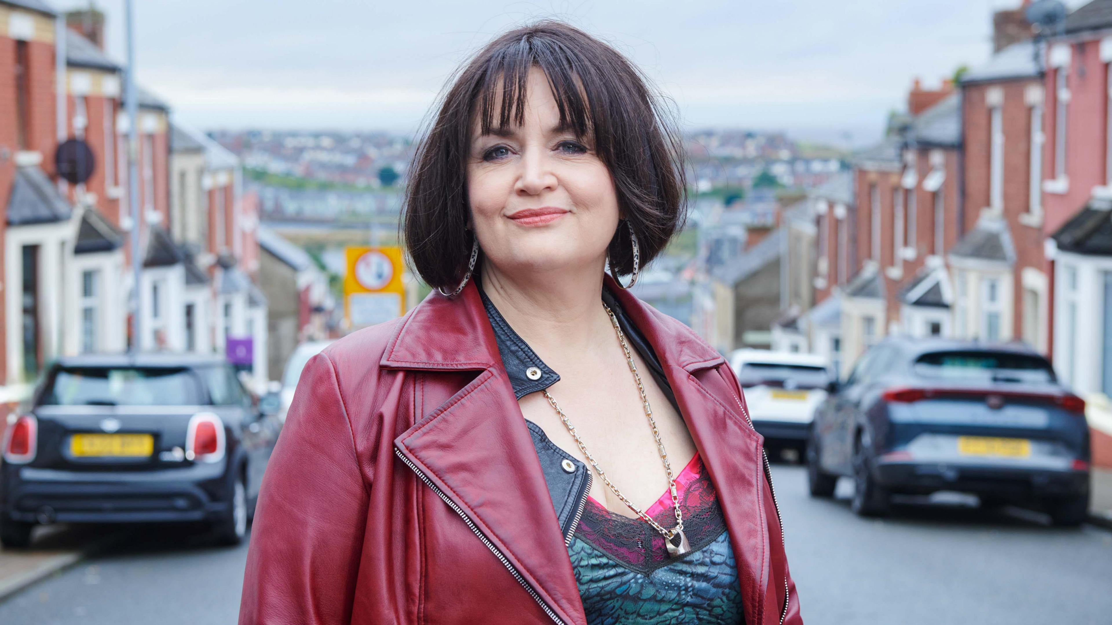 Ruth Jones as Nessa, pictured smiling while wearing a dark red leather jacket on the streets of Barry Island