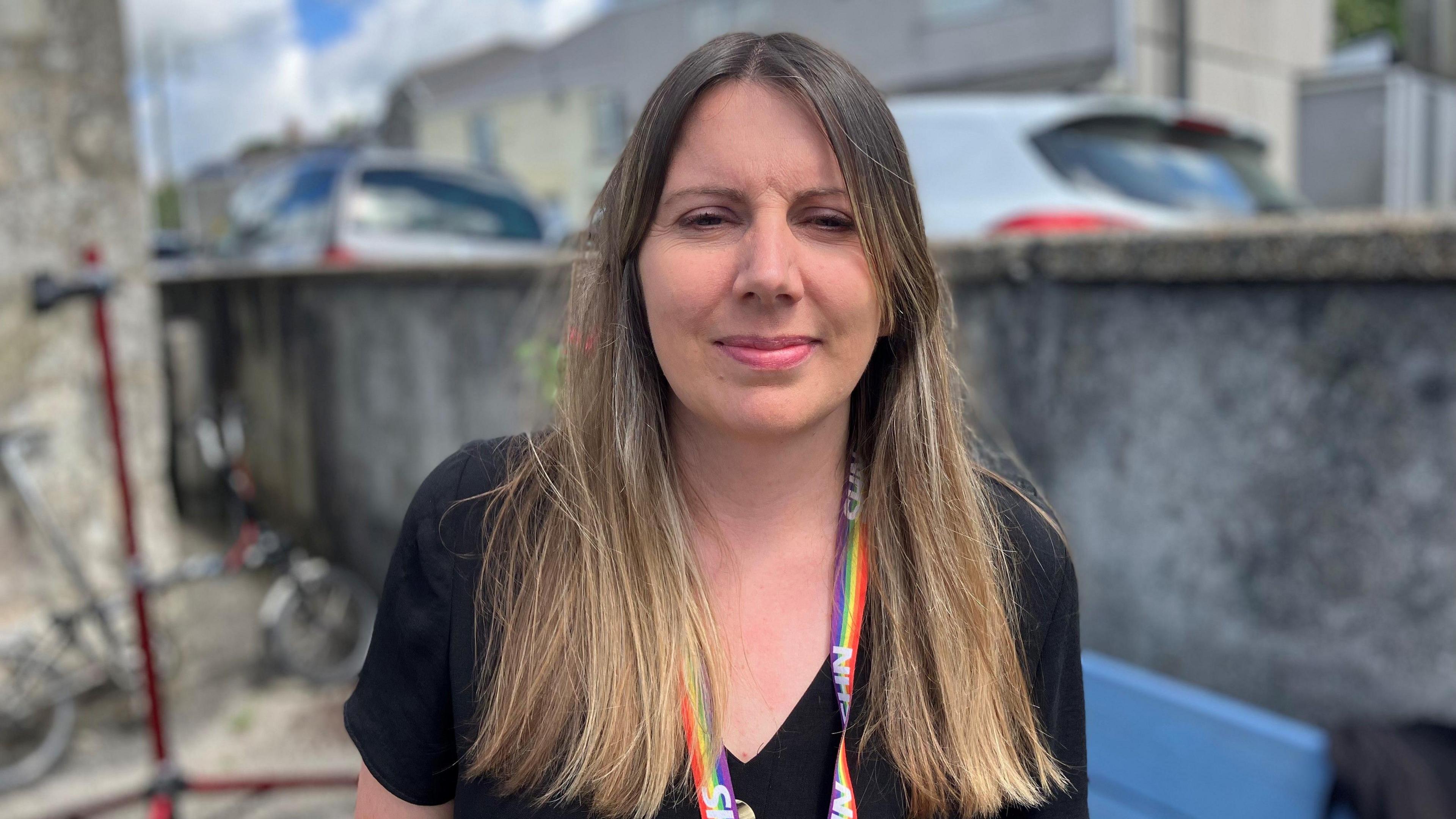 Woman with long brunette hair wearing an NHS lanyard