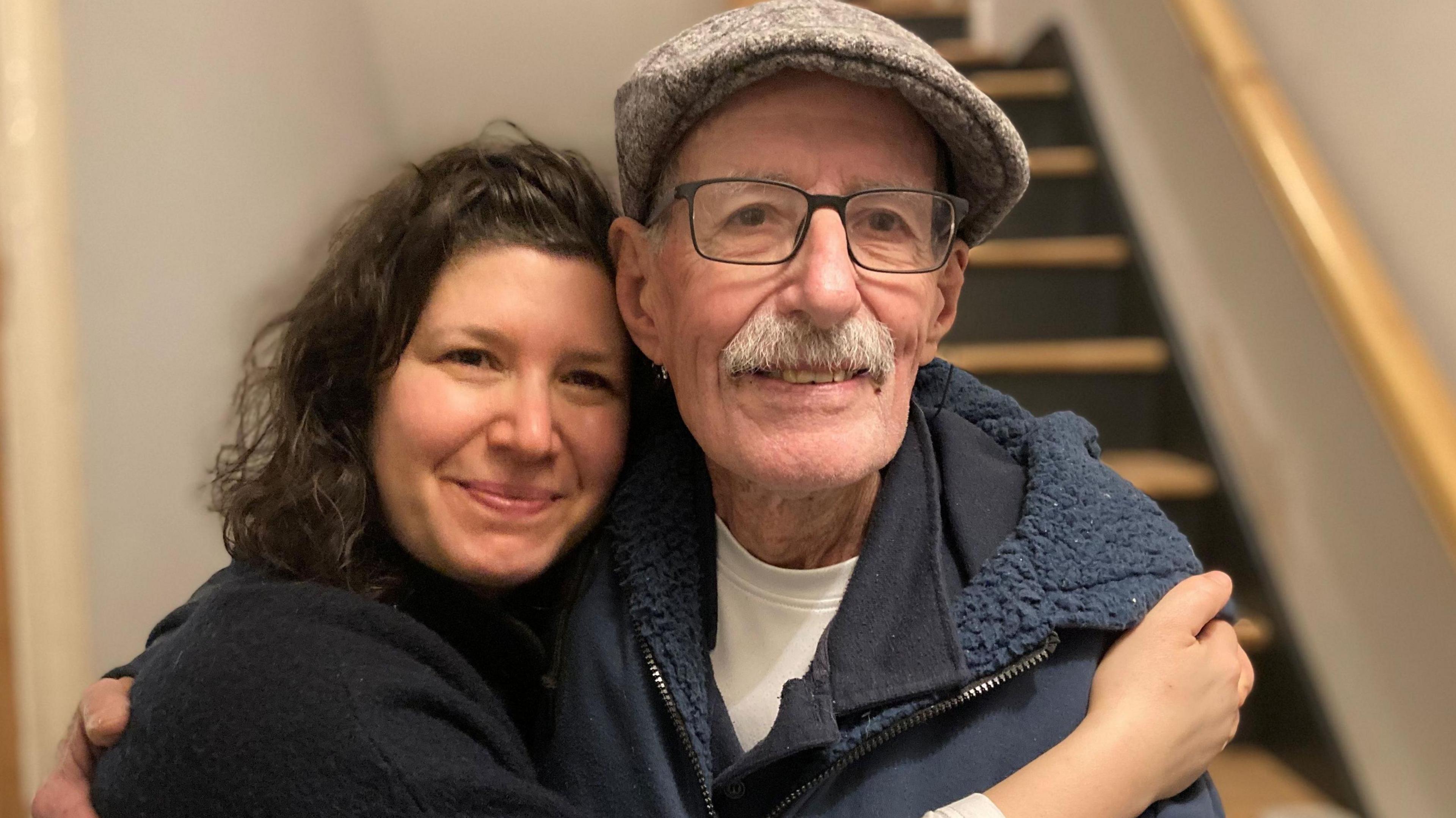 Sharone Lifschitz wears a black jumper and embraces her father, Oded Lifsthiz, who wears a hat and glasses