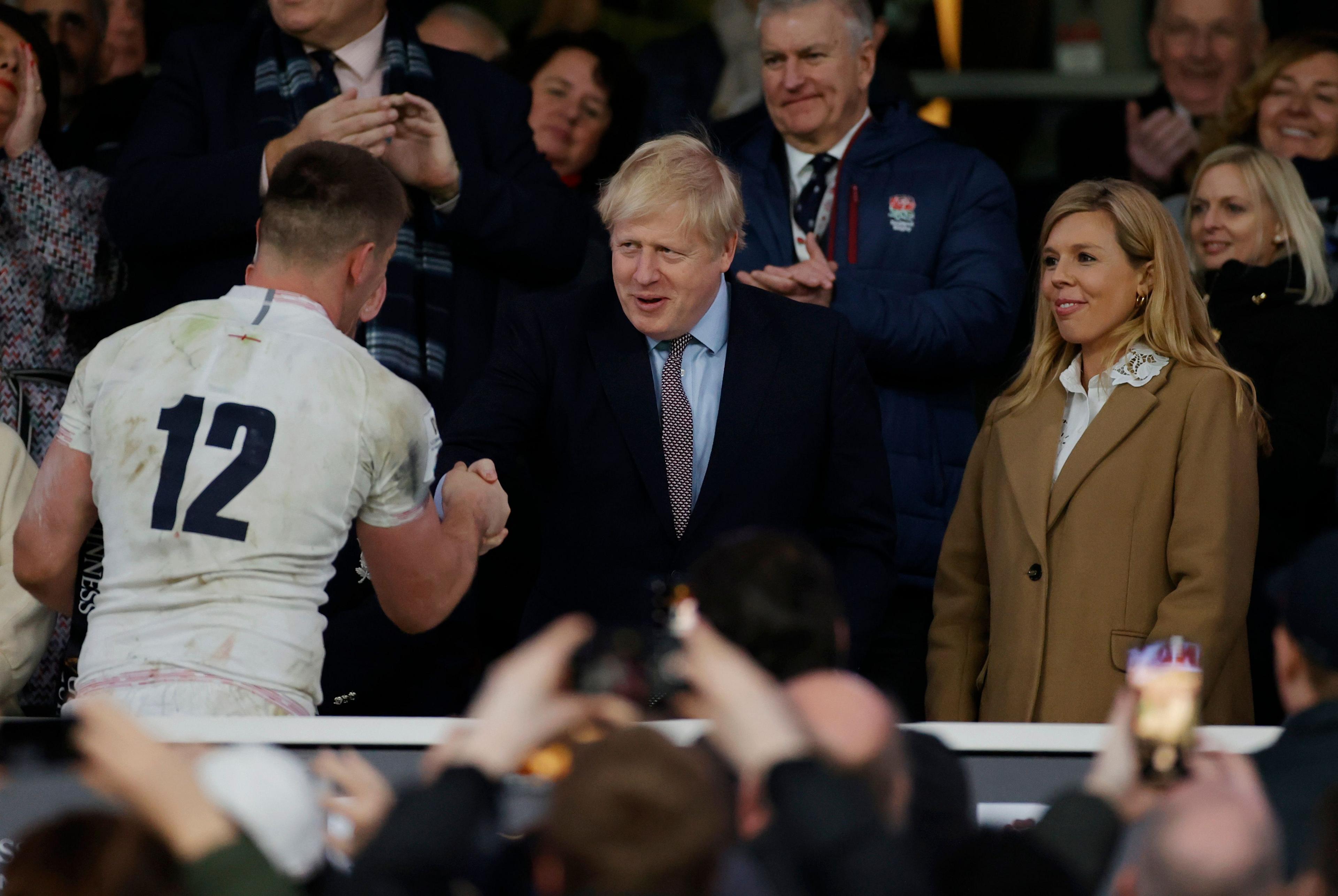 Boris Johnson shaking hands with England captain Owen Farrell at Twickenham on March 7, 2000. Carrie Johnson, now his wife, is standing next to him.