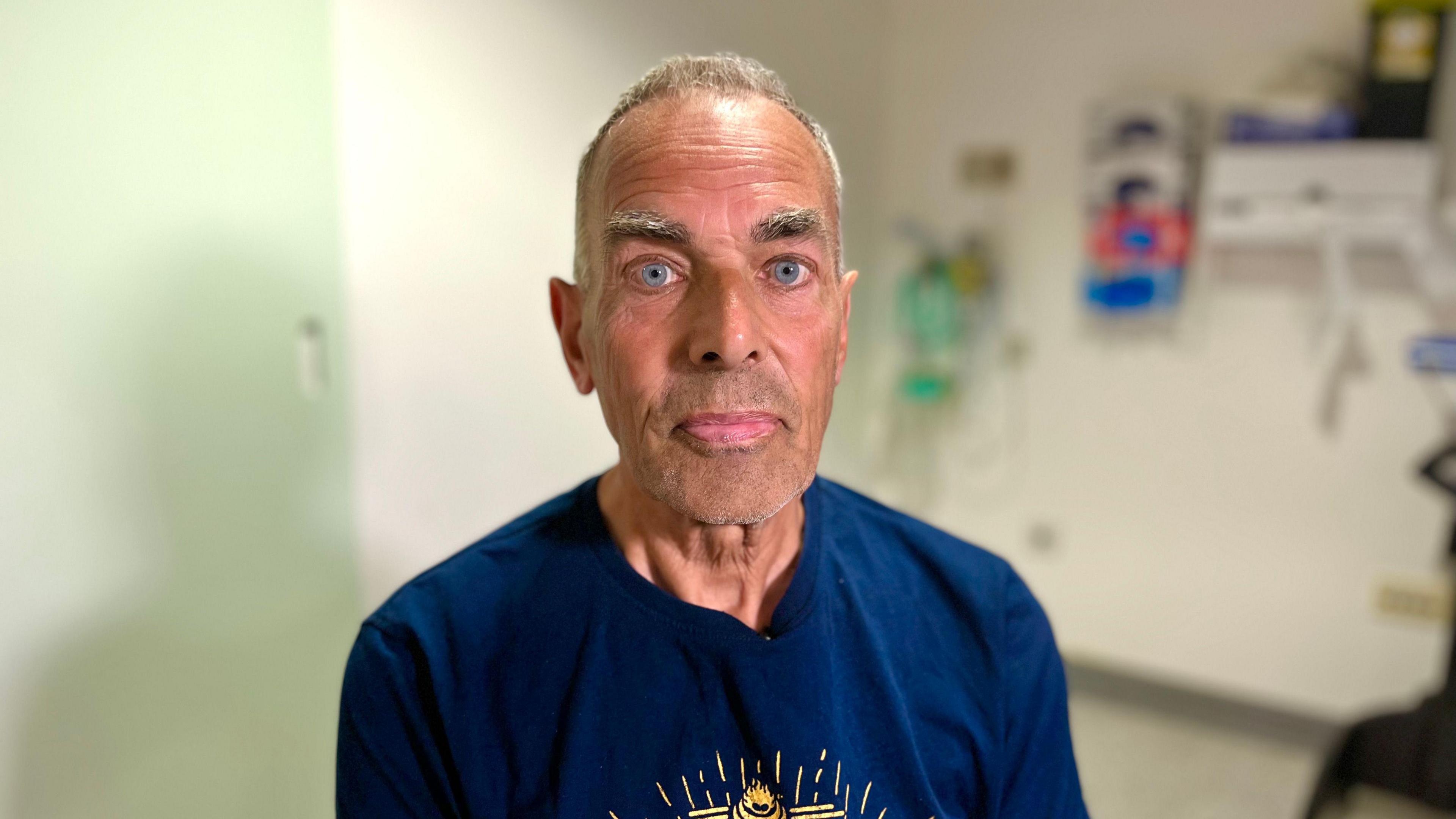 A portrait photo of John Starling in a hospital treatment room and wearing a blue t-shirt