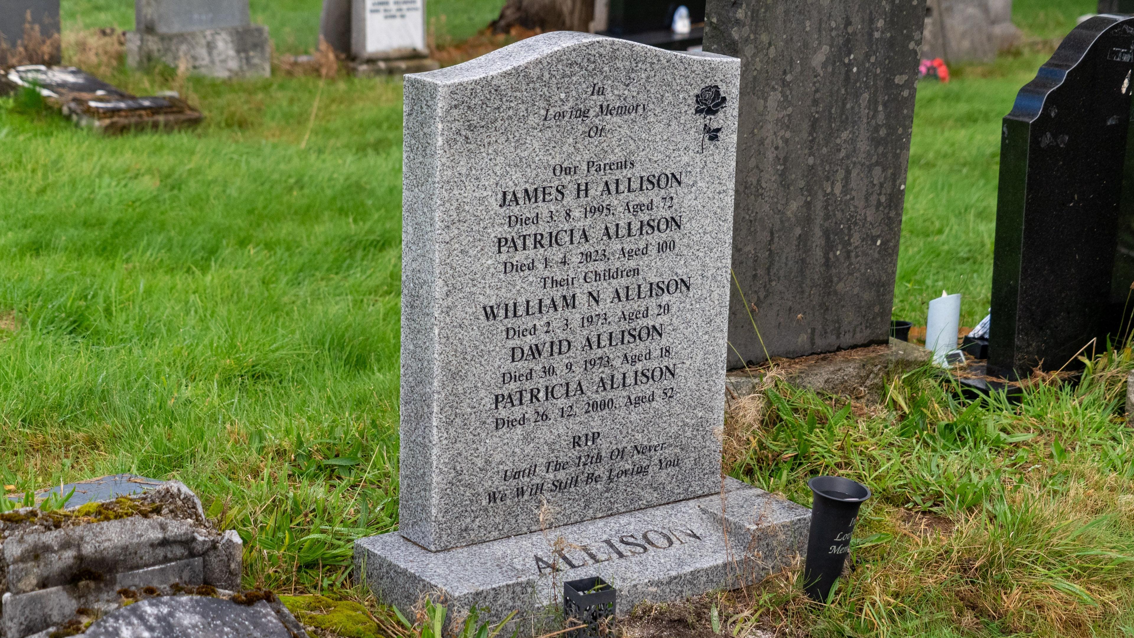 A grey gravestone engraved with the words "In loving memory of our parents, James H Allison, died 3.8.95, aged 72, Patricia Allison, died 1.4.23, aged 100, Their children, William N Allison. died 2.3.74. aged 20; David Allison. died 30, 9, 73 Aged 19; Patricia Allan. Died 26.12. 2000, aged 52".RIP. "Until the 12th of never, we will still beloving you."