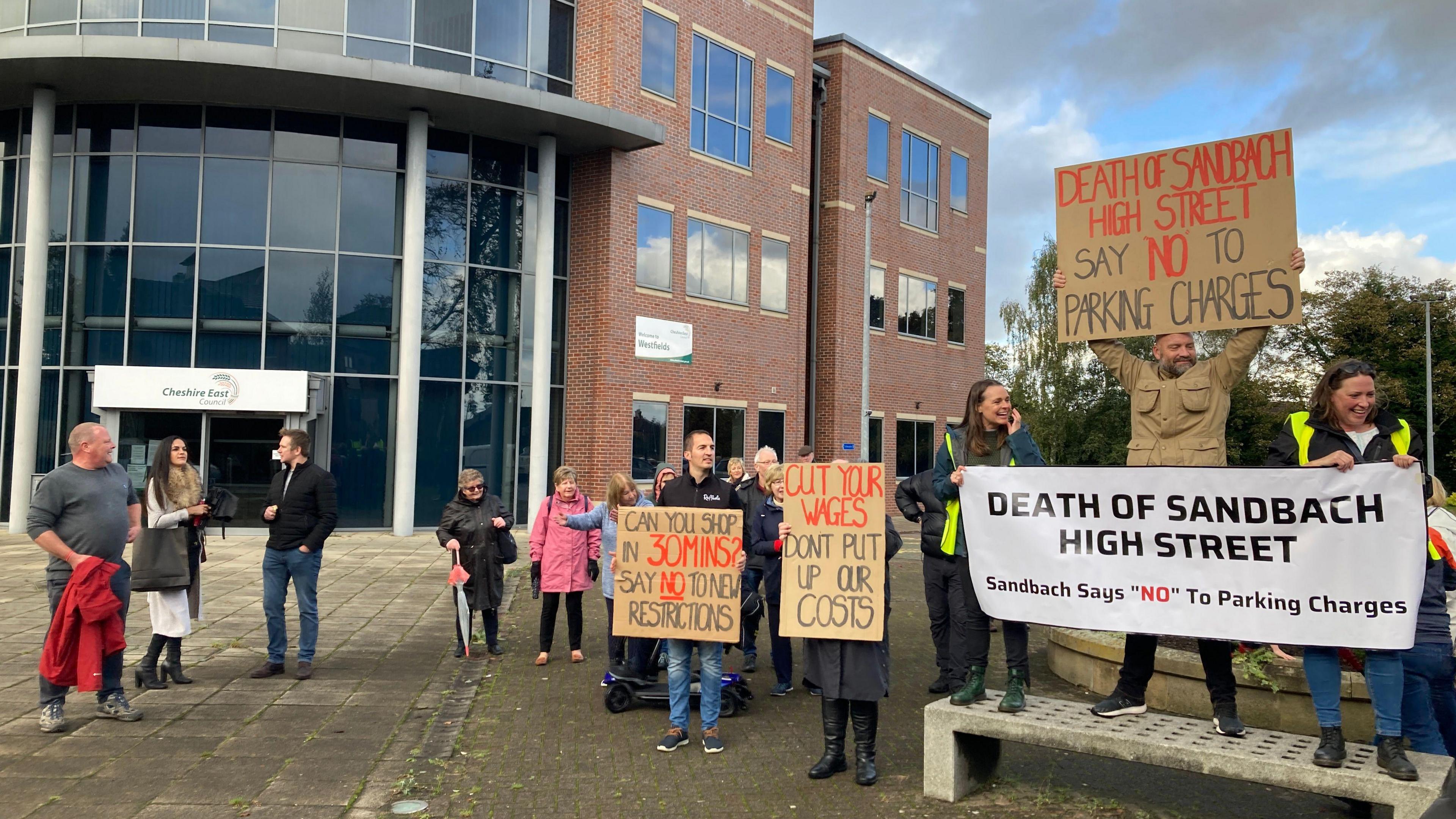 Protestors holding signs protesting against parking charges in Sandbach outside Cheshire East Council's offices at Westfields in Sandbach