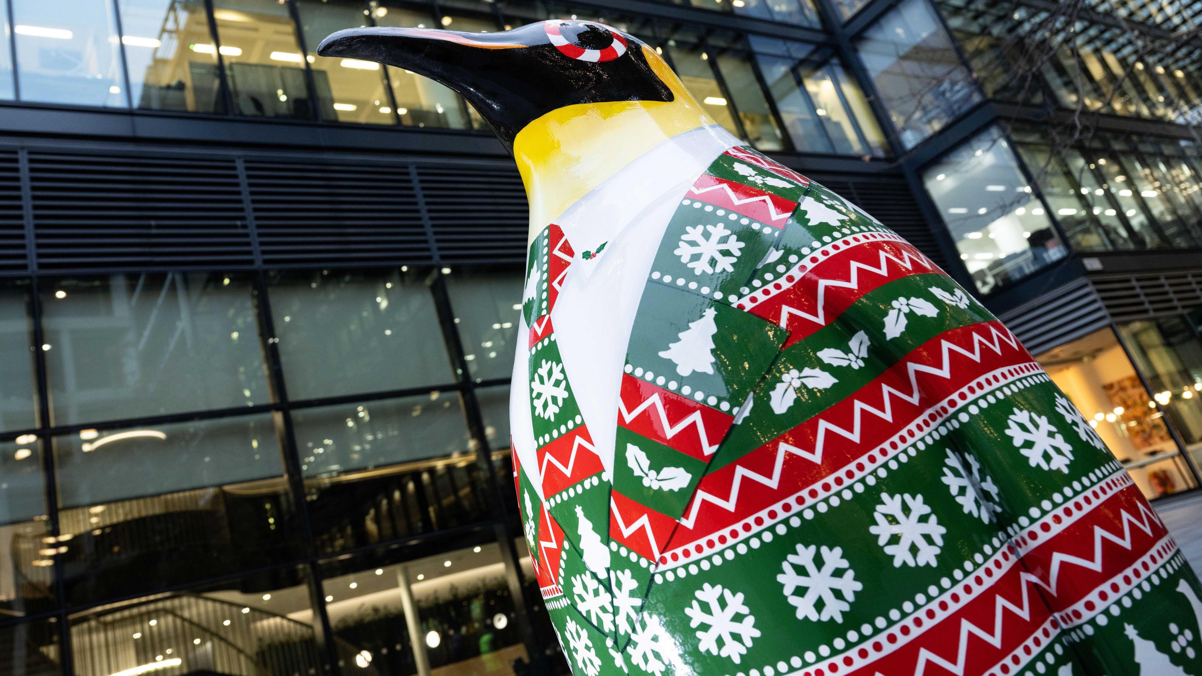 Penguin statue in green and red festive suit with snowflakes and Christmas trees