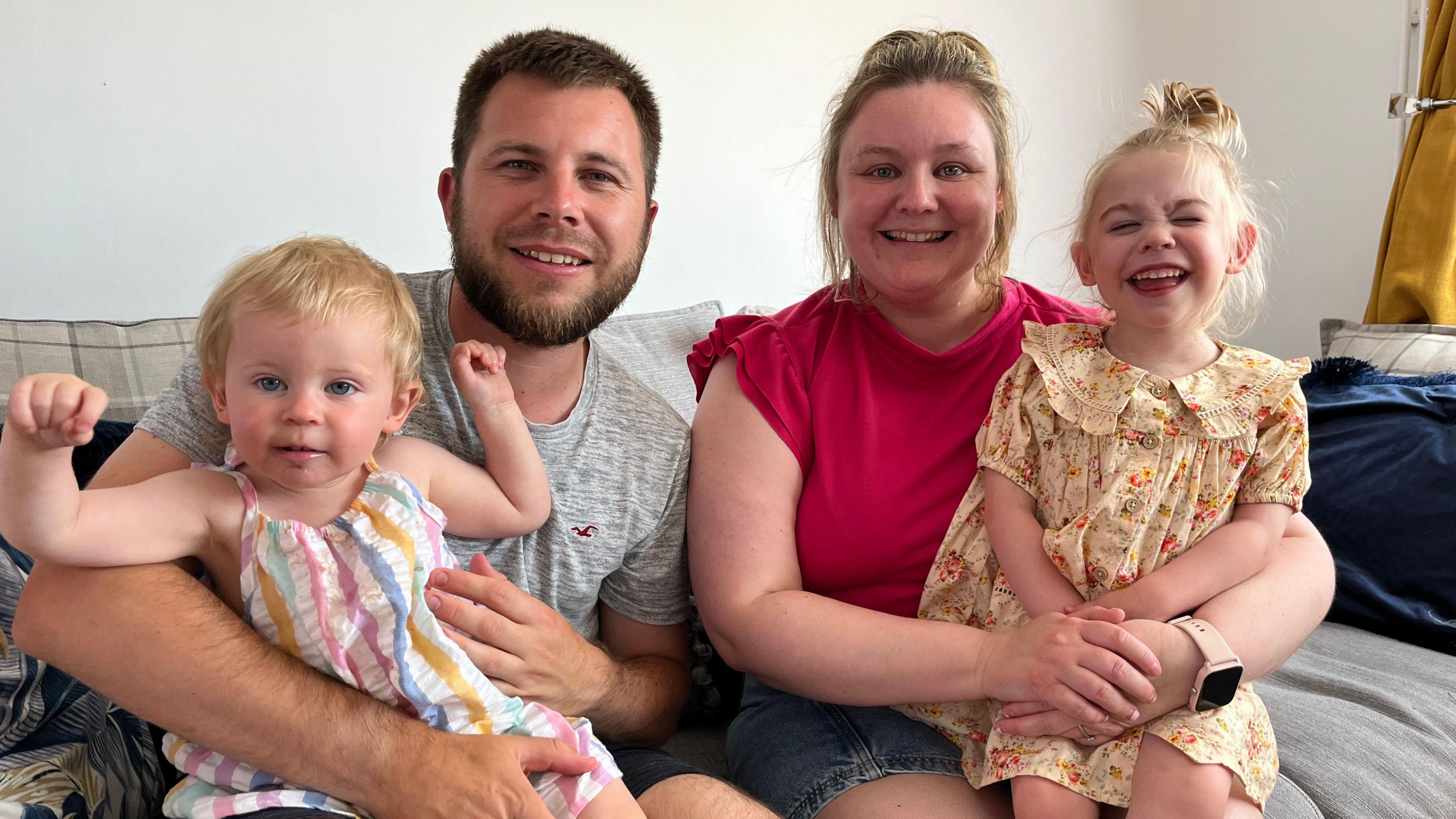 Rich Bolter, Jodie Woolford, Amelia (R) and Blossom (L) look into the camera smiling as they sit on their sofa at home