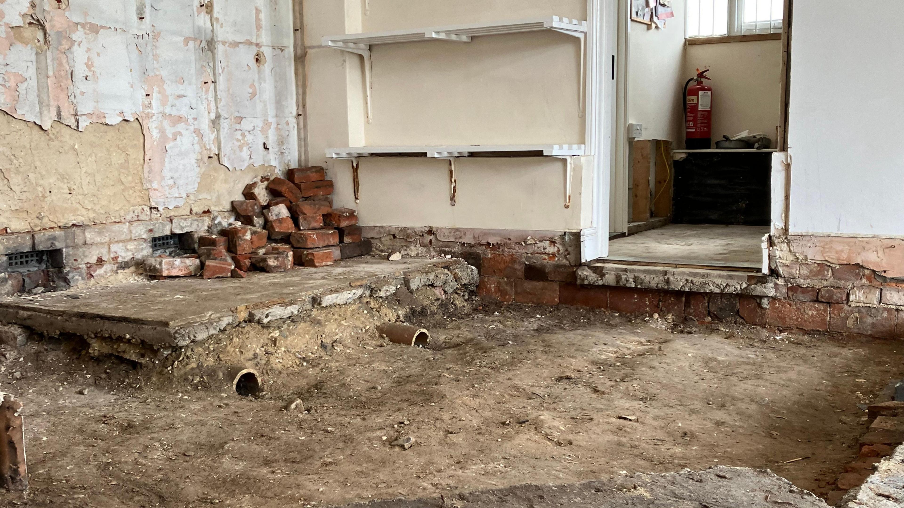 Interior of shop showing flood-damaged, bare dirt floor and bricks piled up in a corner