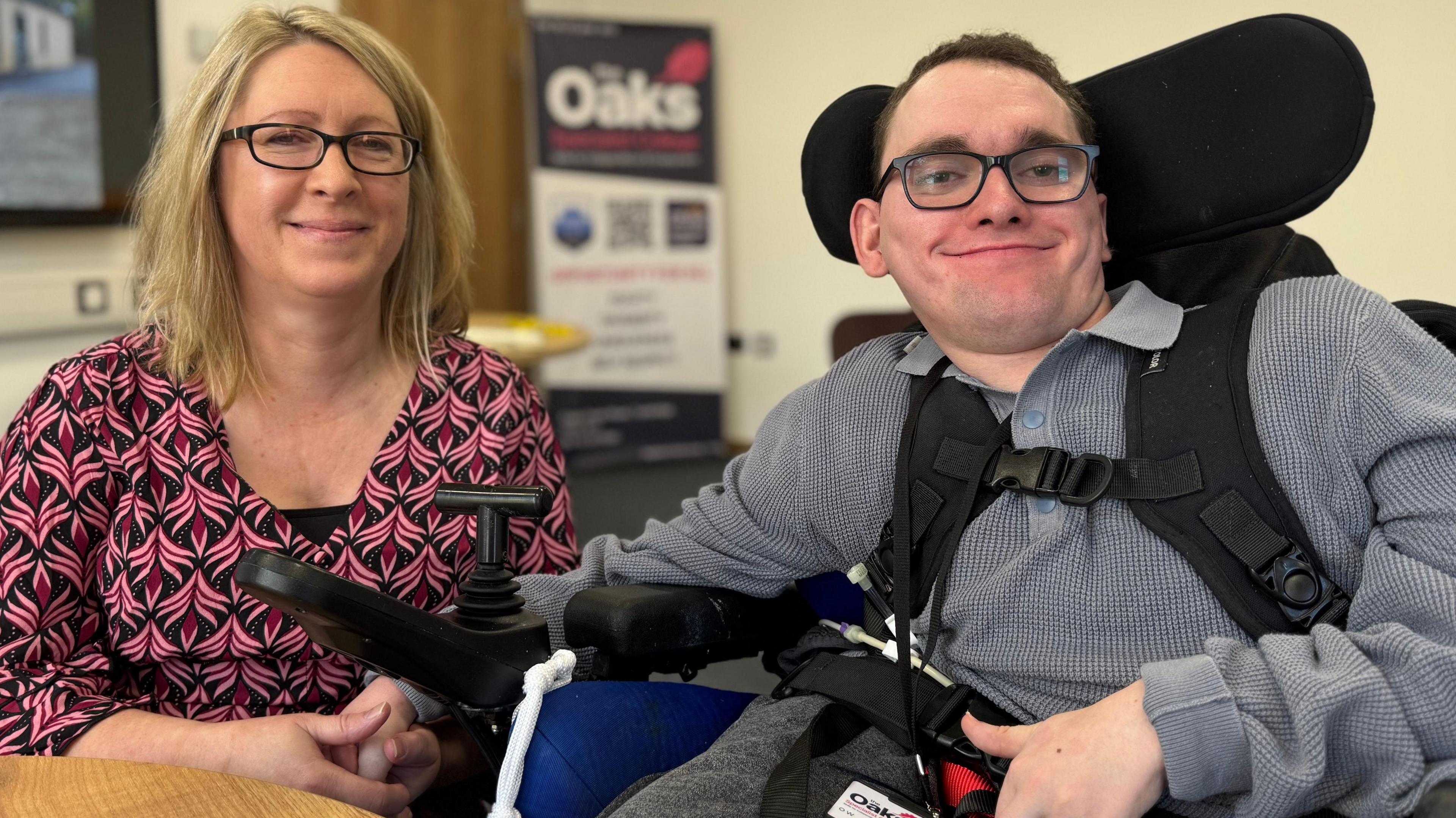 A picture of Louise and son Oliver at the new SEND college in Tonbridge, Kent. Louise is wearing a pink and black dress and Oliver, who is in a specialist chair with a headrest, is wearing a grey shirt. 