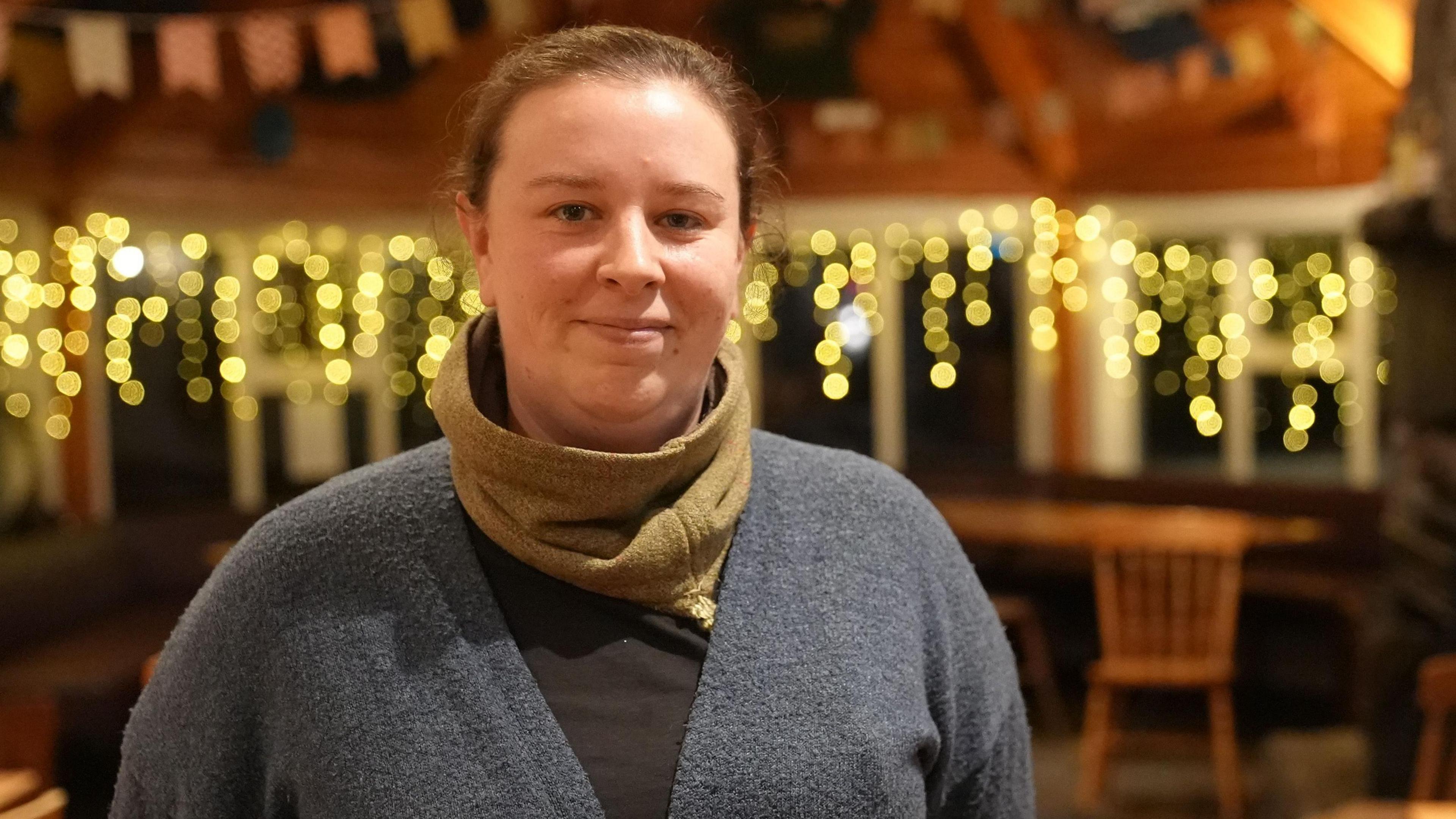 Stephanie Harris inside the Old Forge pub, which has stone walls, wooden beams ands fairy lights. She has tied-back brown hair and is wearing a grey cardigan, brown top and khaki snood.