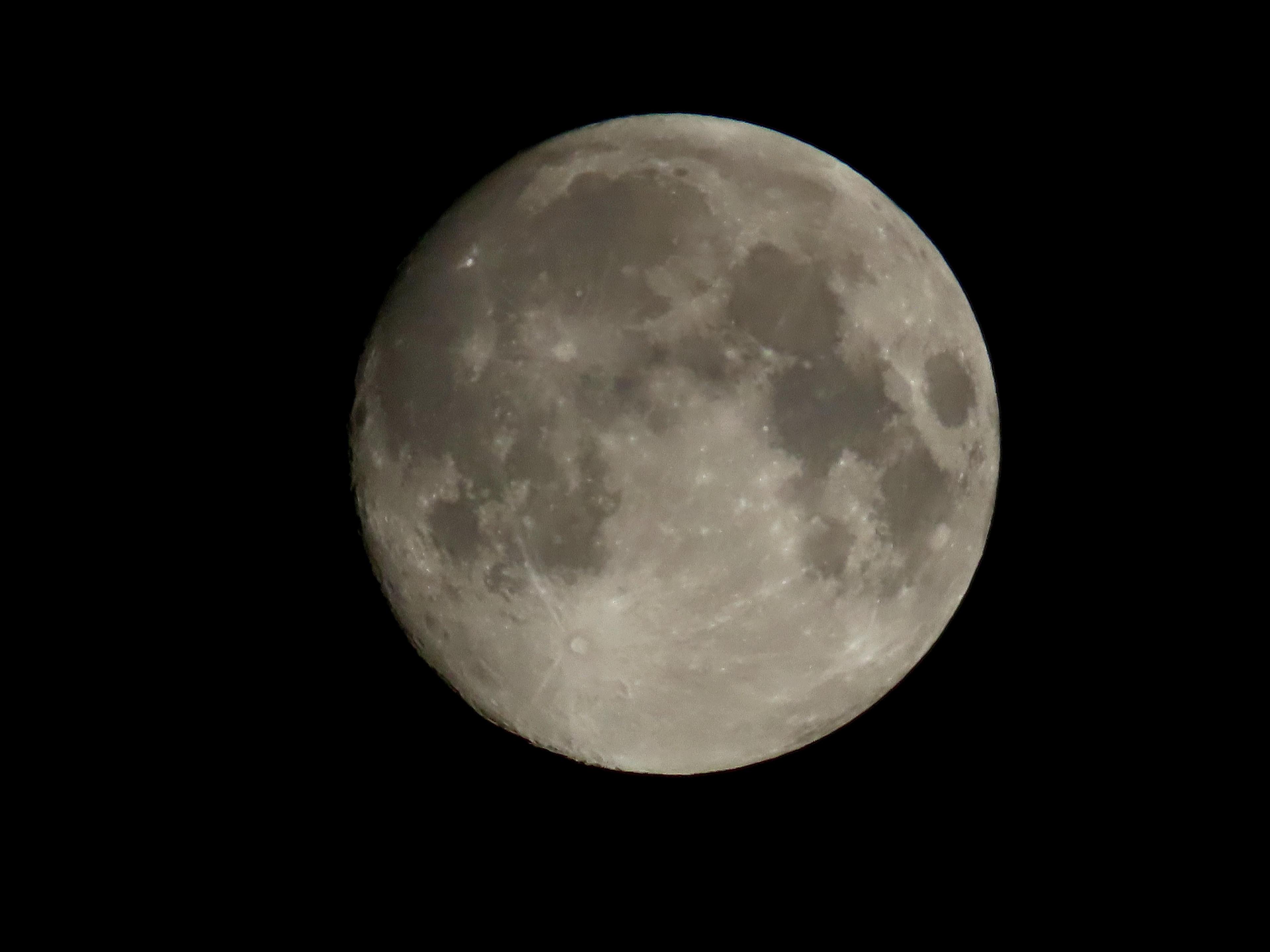 The moon fills the shot against a pitch-black sky. Light and dark features of the lunar terrain are visible including crater chains, mountains and valleys. 