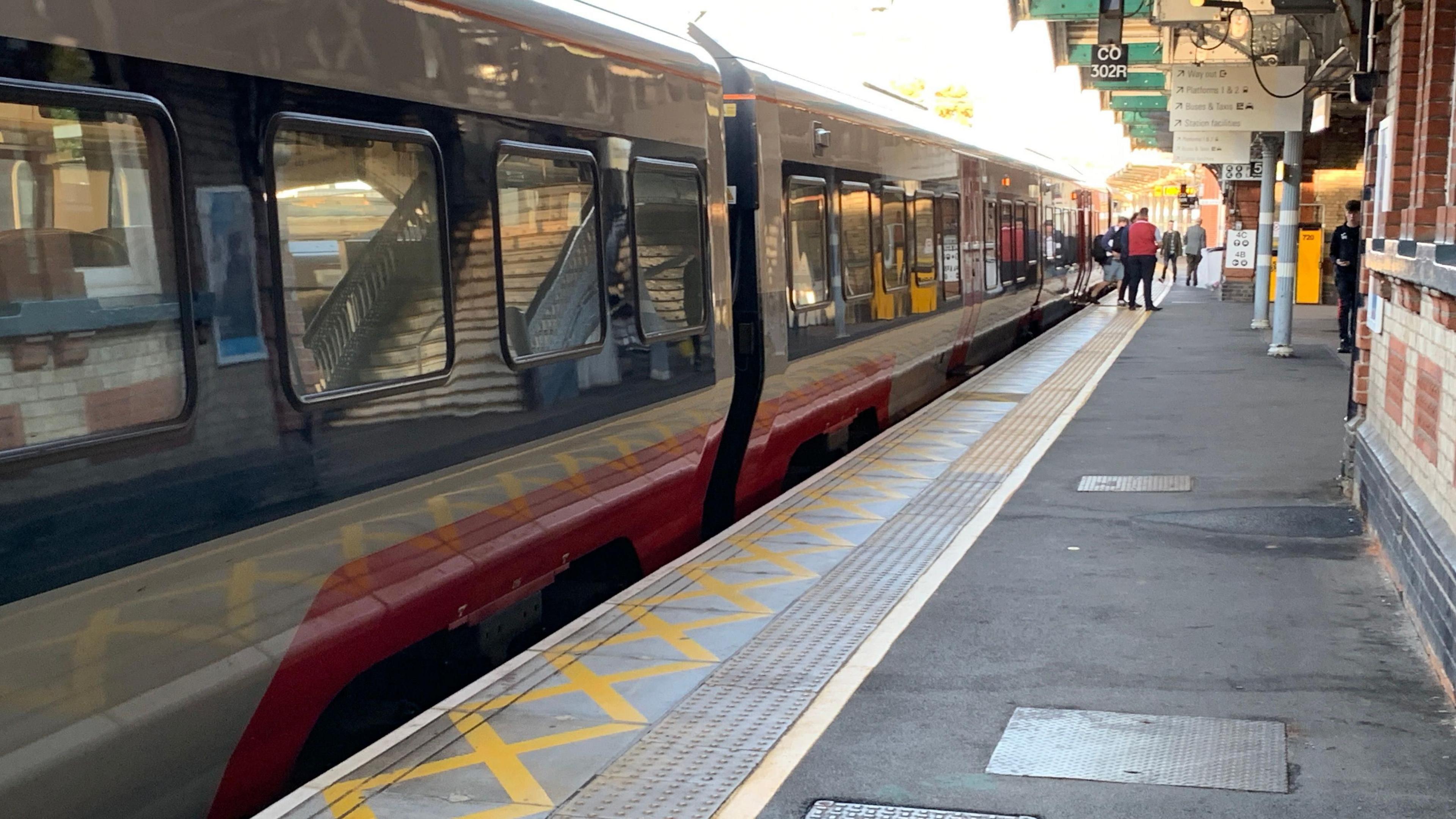 General view of Ipswich station's platform four showing a train on the left and staff and members of the public in the distance.
