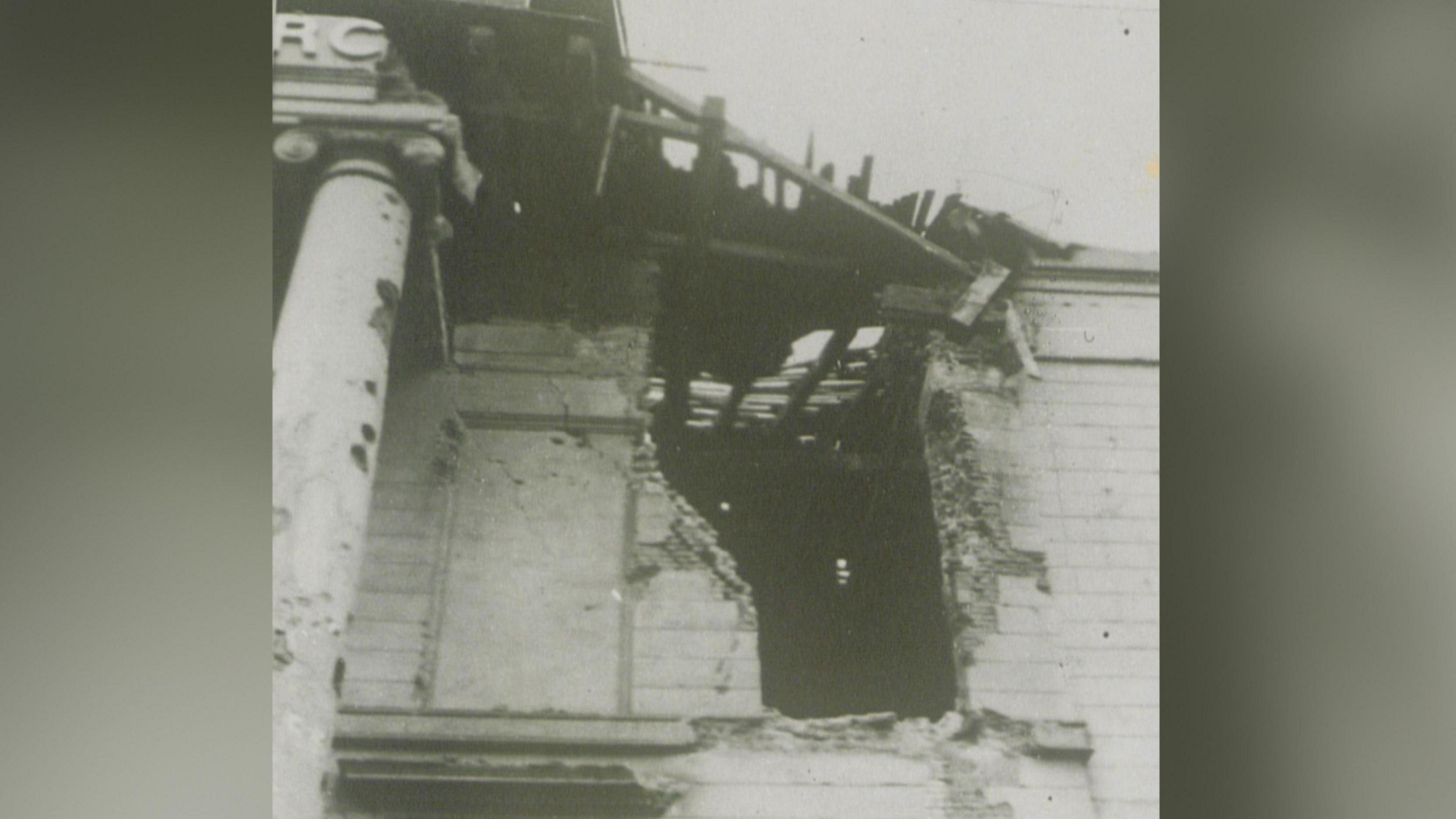 In a black and white photograph we get a brief insight into the damaged caused to the church during the bombings of World War Two. Pictured is a large hole in the side of the building as well as exposed wood in the roof.