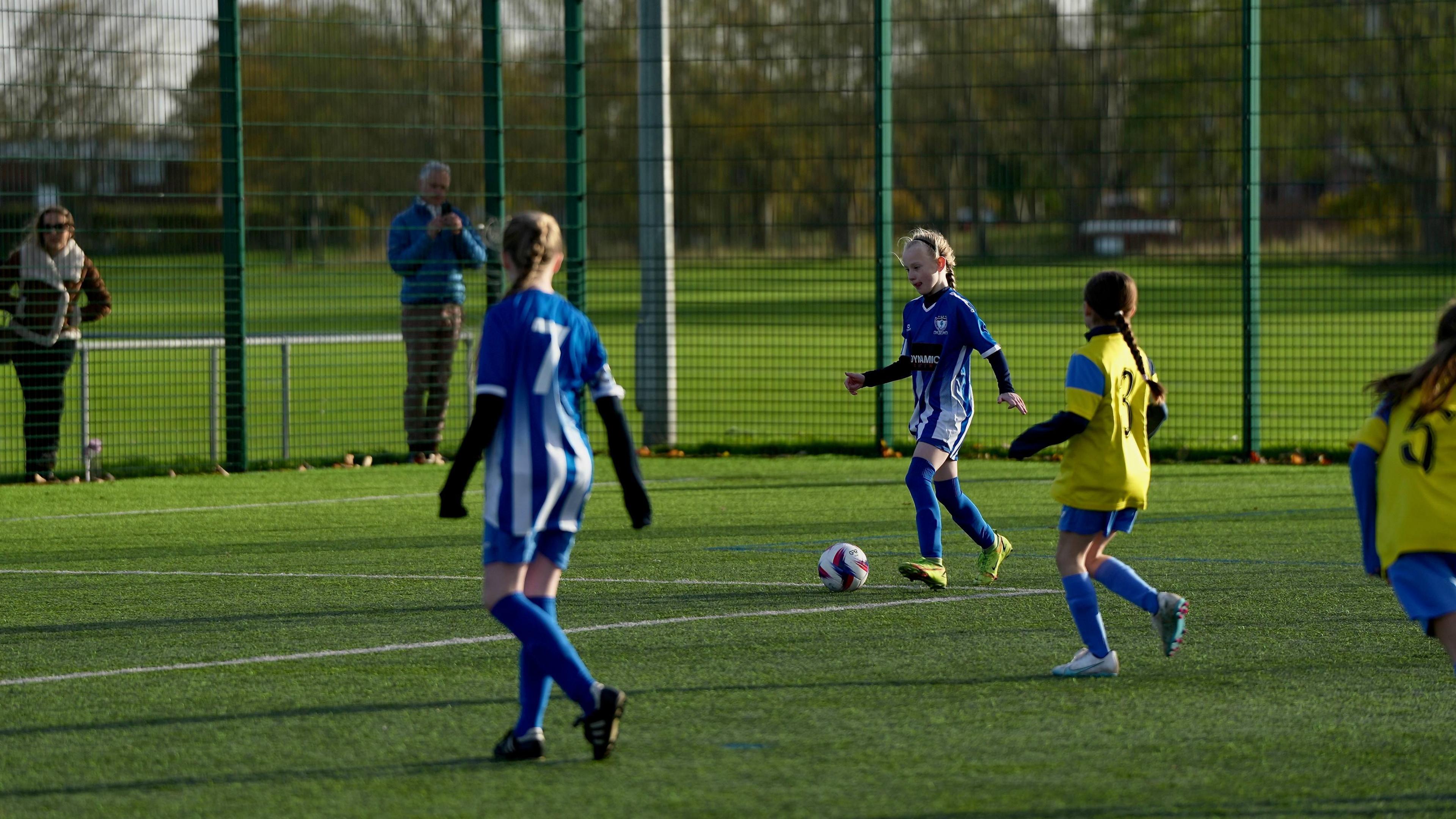 Four girls wearing the colours of Whitley Bay Football Club and Whitley Bay Sporting Club play on an artificial pitch.