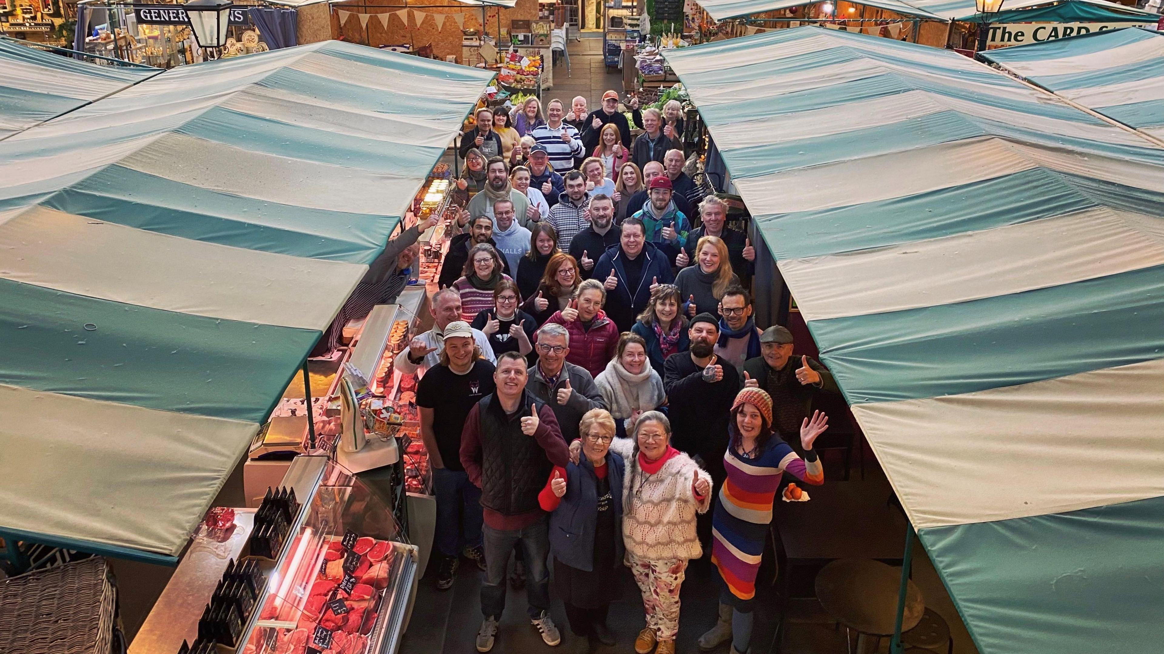 A large gathering of people seen from above, between two rows of covered stalls with striped coverings