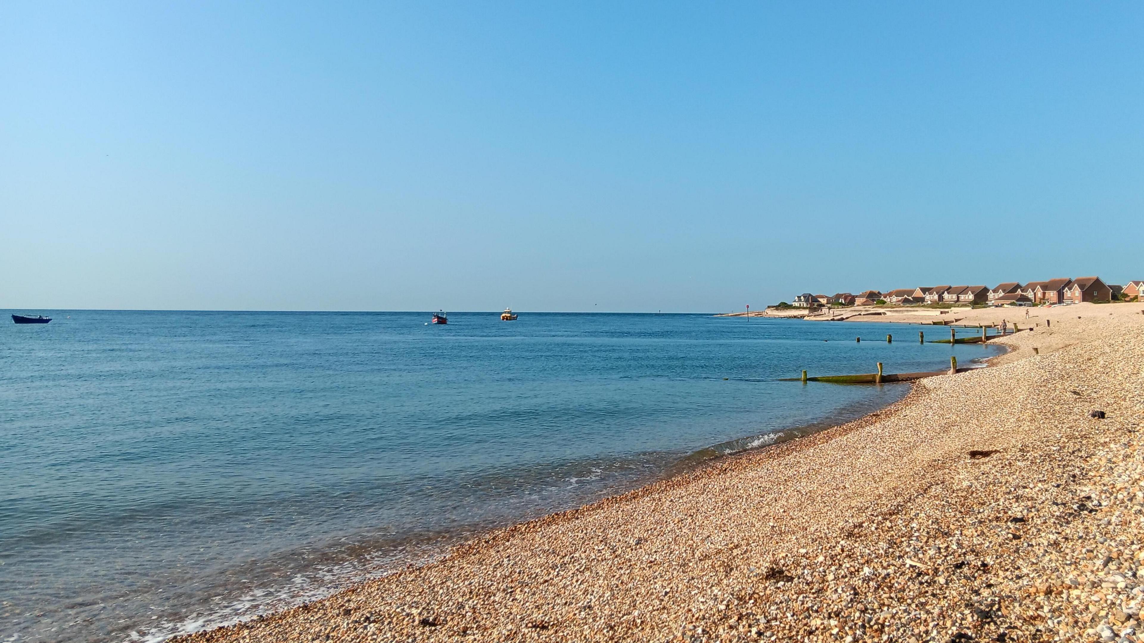 A sunny beach with groynes and a cliff in the distance - it's a sunny day without a cloud in the sky