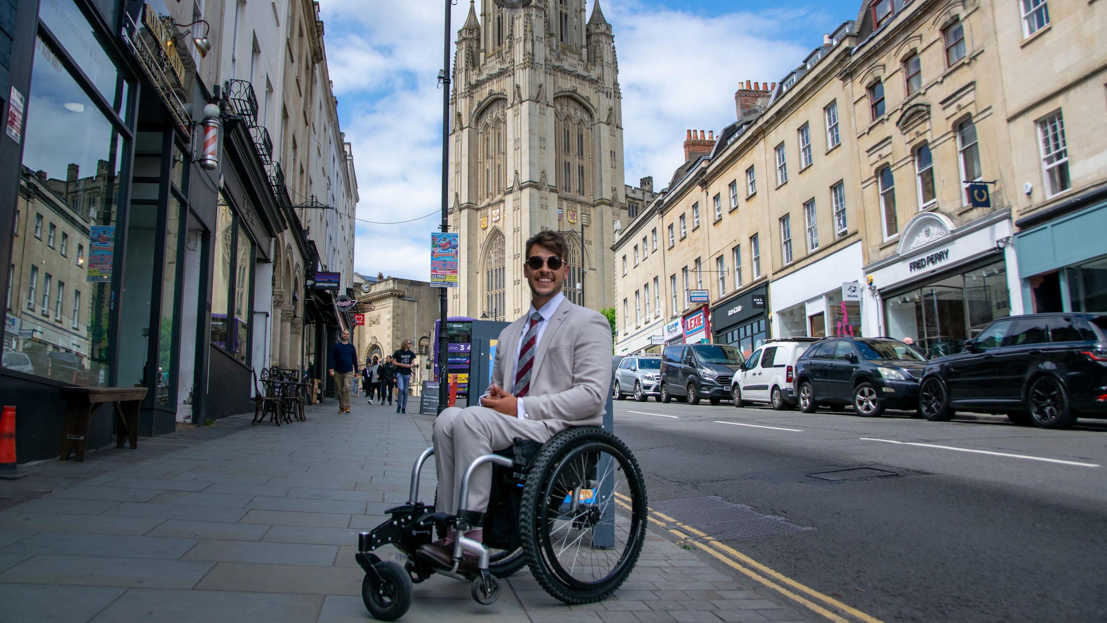 Xander Van der Poll sitting at the top of Park Street in Bristol. He is in a wheelchair and smiling at the camera