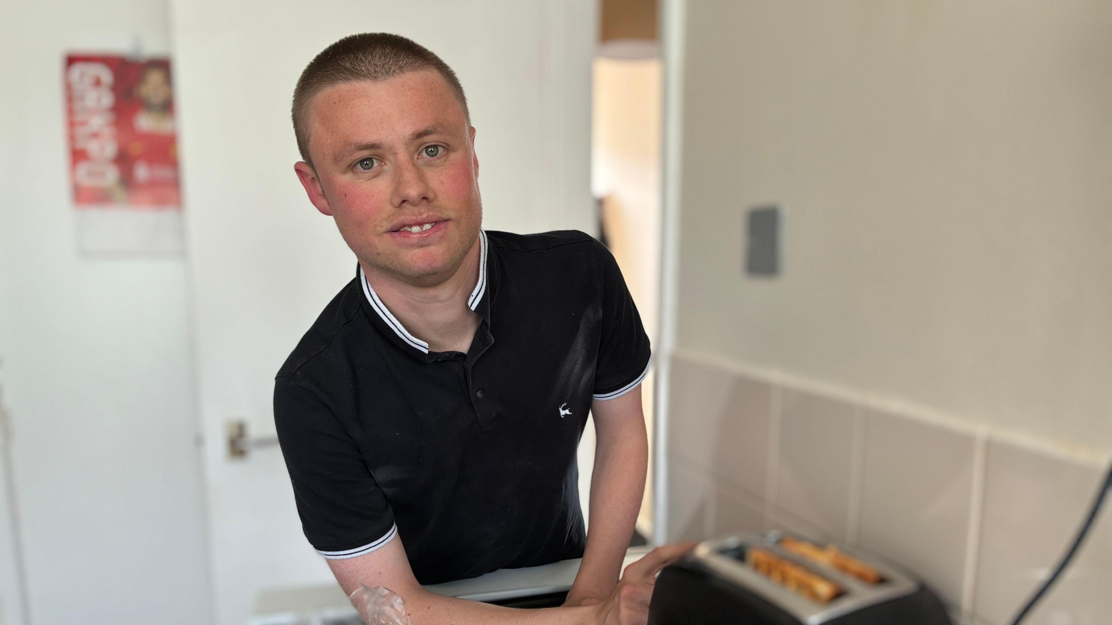 Nathan Huntley wears a black polo-shirt and is pictured in a kitchen putting waffles into the toaster.