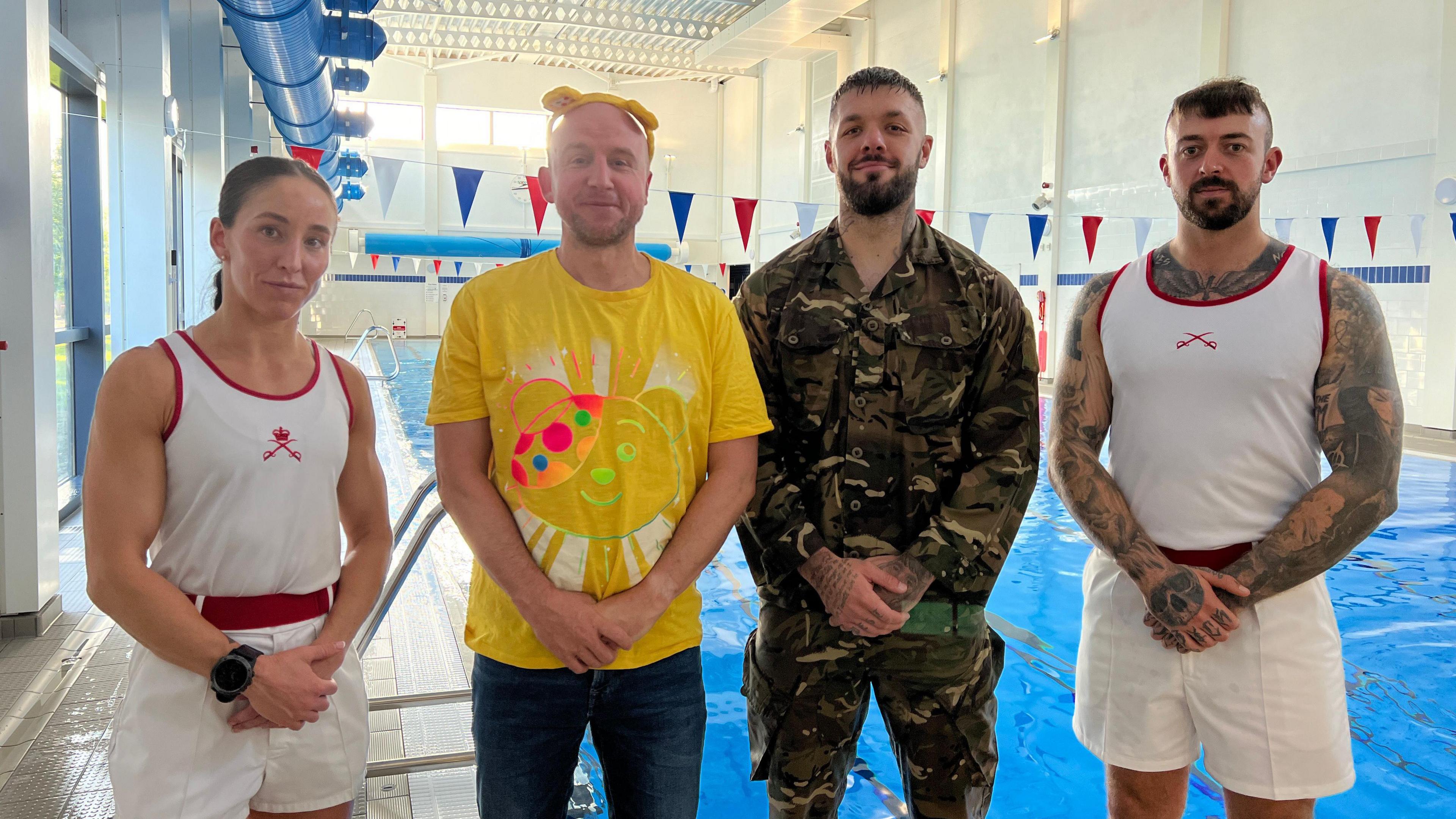 Three men and a woman stood in front of a swimming pool. The woman and one of the men are dressed in military sports clothing. One of the men is in army camouflage and the final man is Ben Prater, BBC Wiltshire's breakfast show presenter. He is wearing a yellow children in need t-shirt.