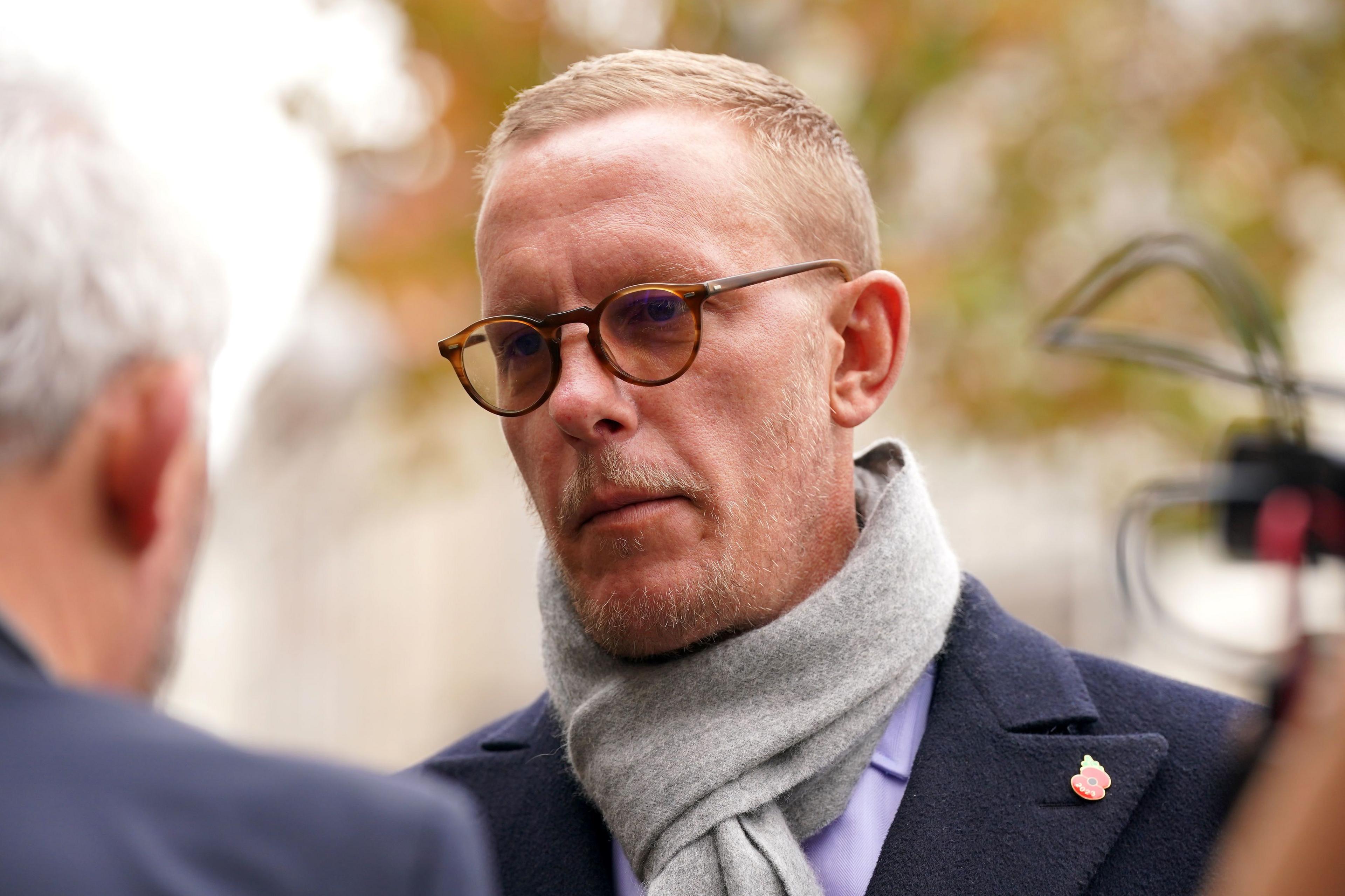 Head and shoulders image of Laurence Fox wearing a dark coat, purple shirt and grey scarf