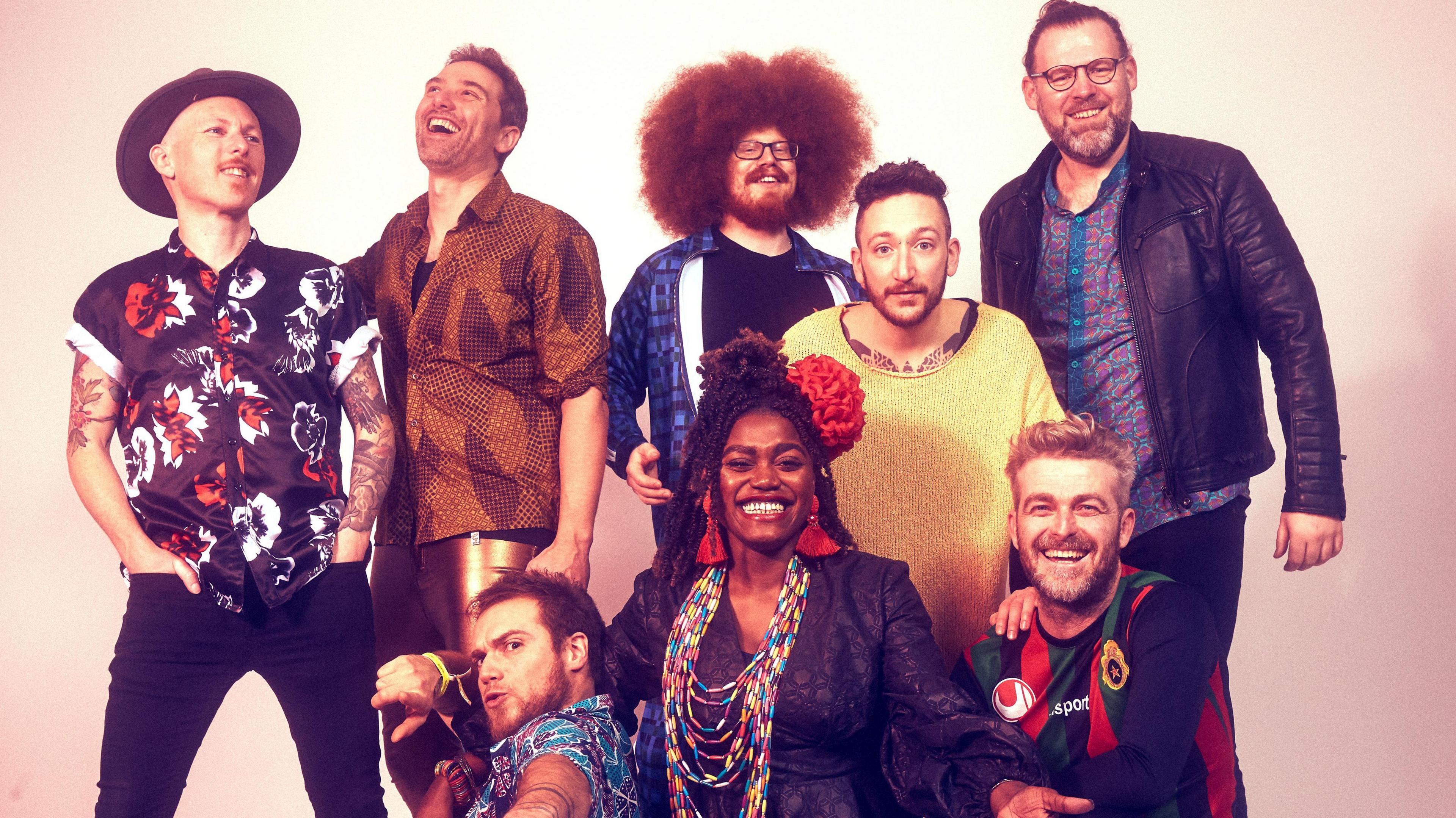 The band are a bohemian-looking bunch, posing, smiling and laughing for a group picture.