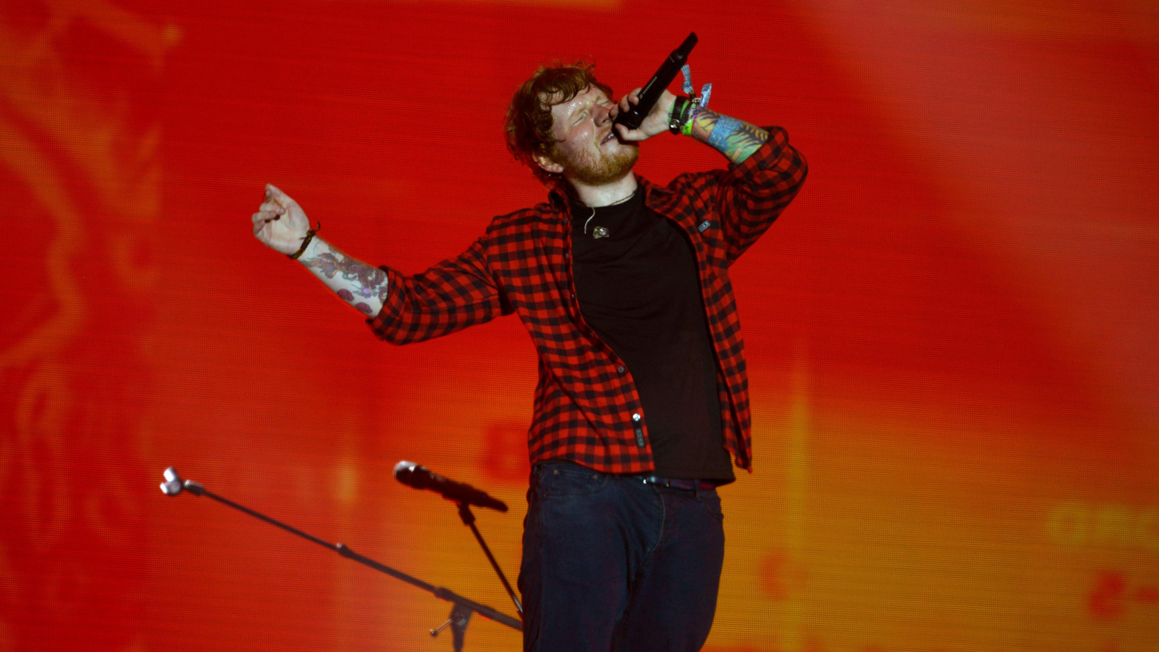 Ed Sheeran stands with eyes closed with microphone raised to mouth