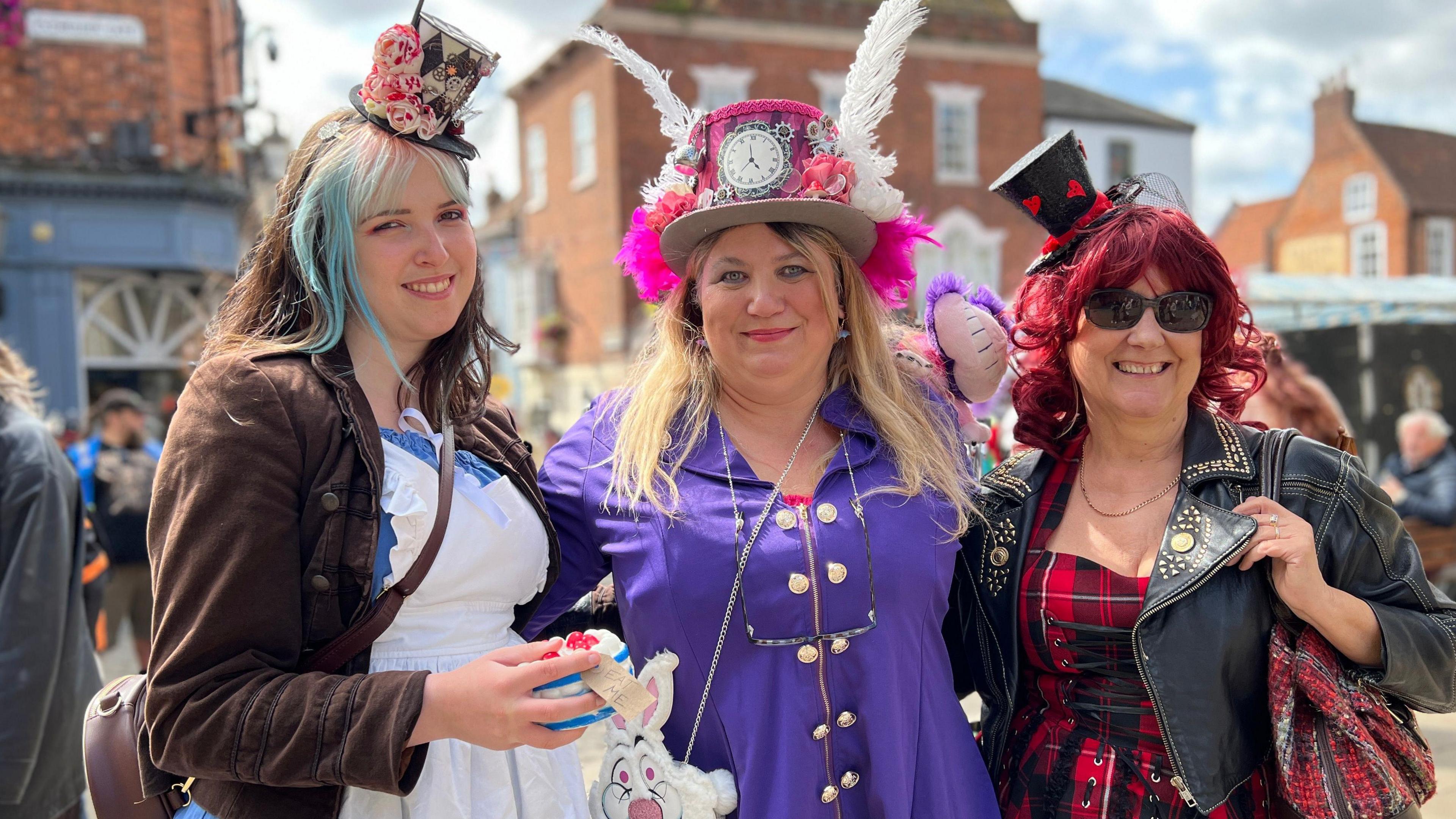 Three women showing off their steampunk outfits which comprise of brightly-coloured hats - one with a clock face in the centre