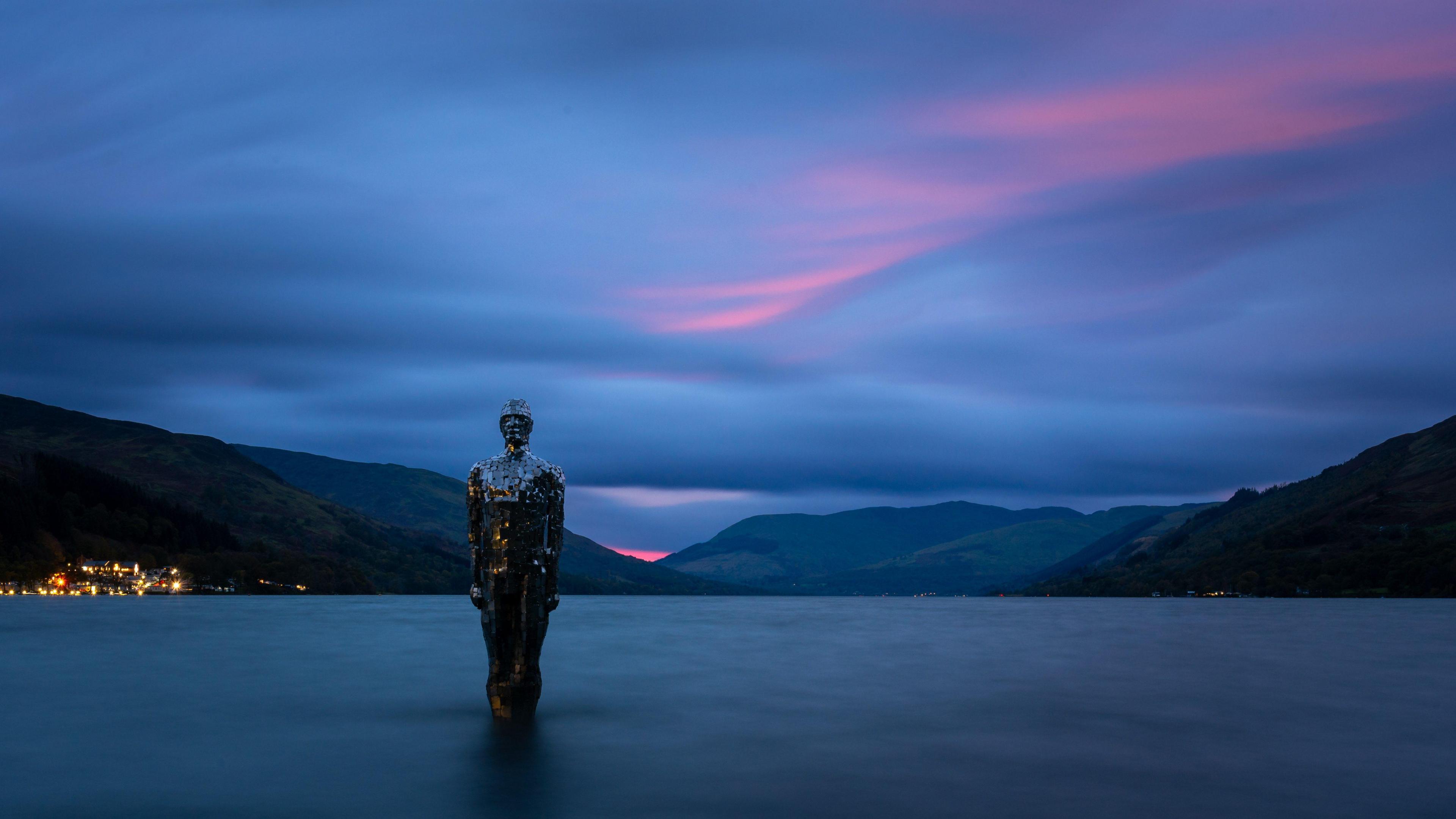 Dark water surrounds the statue which is made from mirrors.