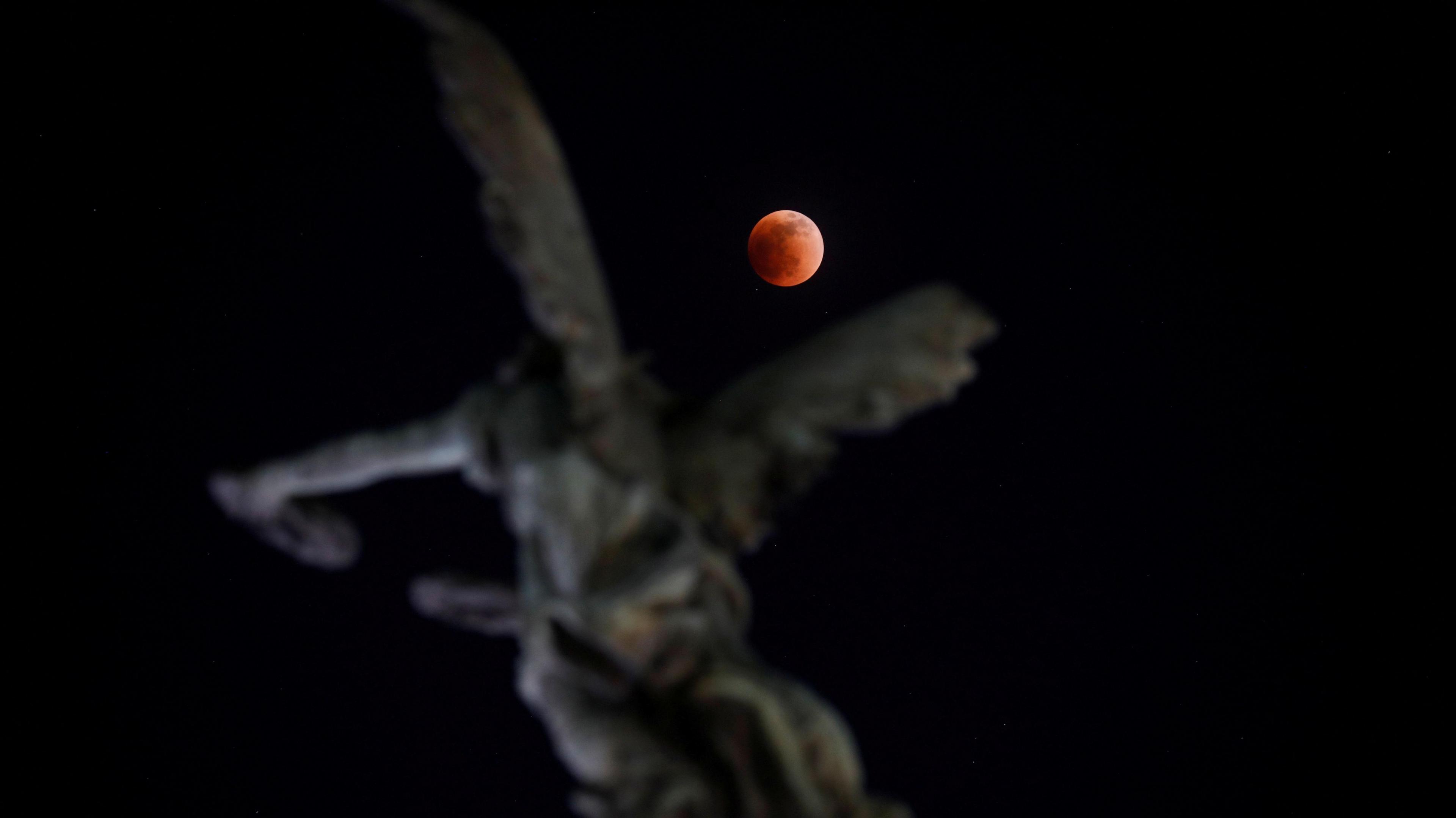 blood moon framed by a statue