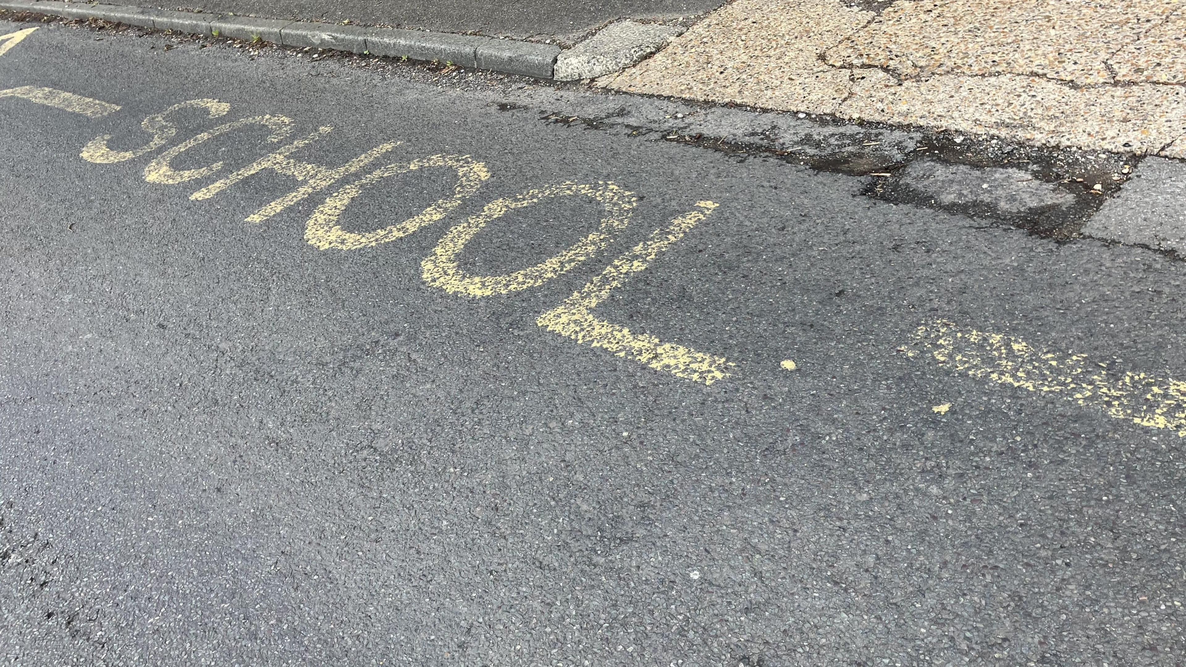 Faded yellow writing on the road saying school