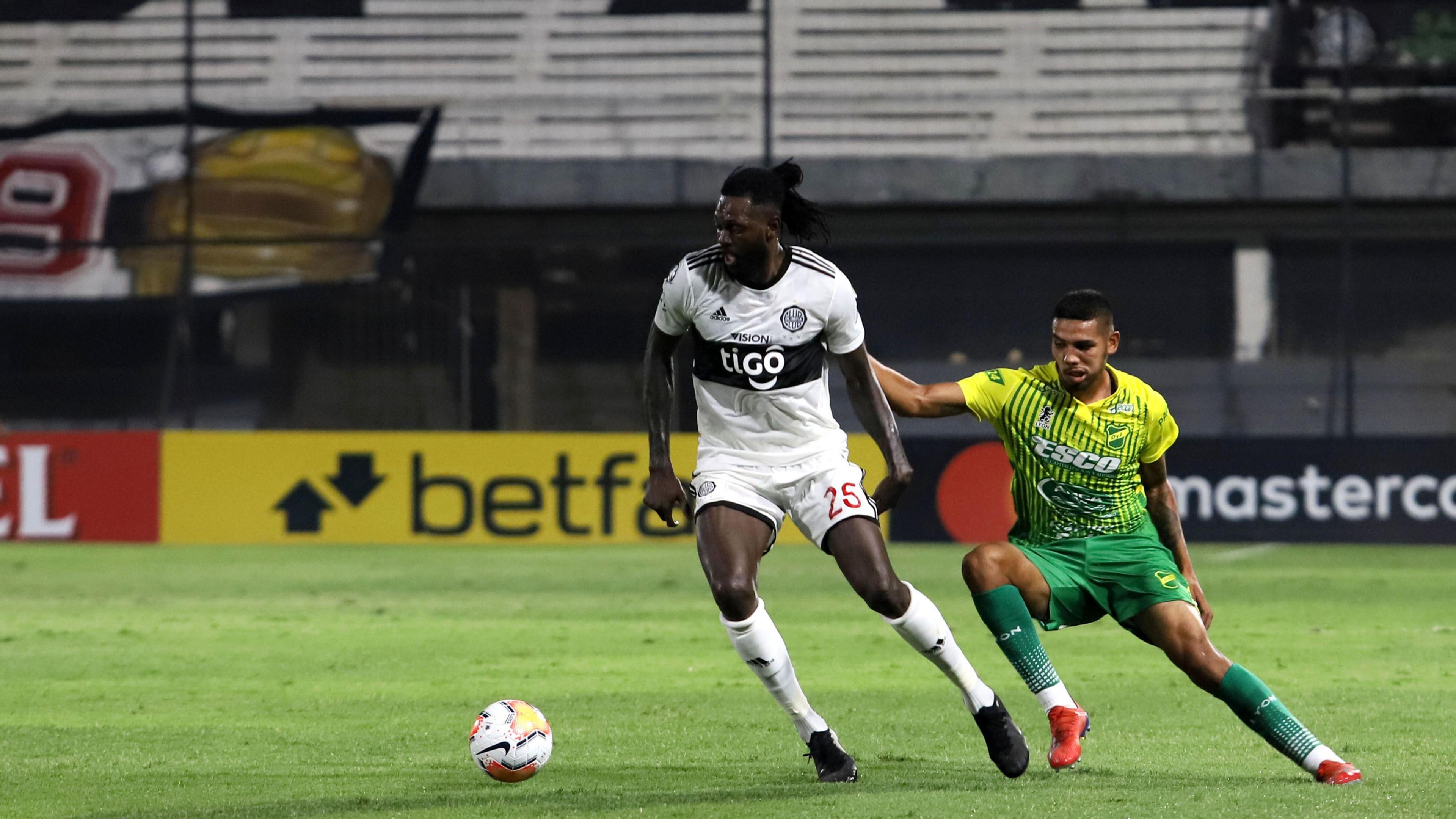 Emmanuel Adebayor, wearing a white stripe with a black horizonal stripe, controls the ball while a defender wearing green an yellow attempts to get to the ball