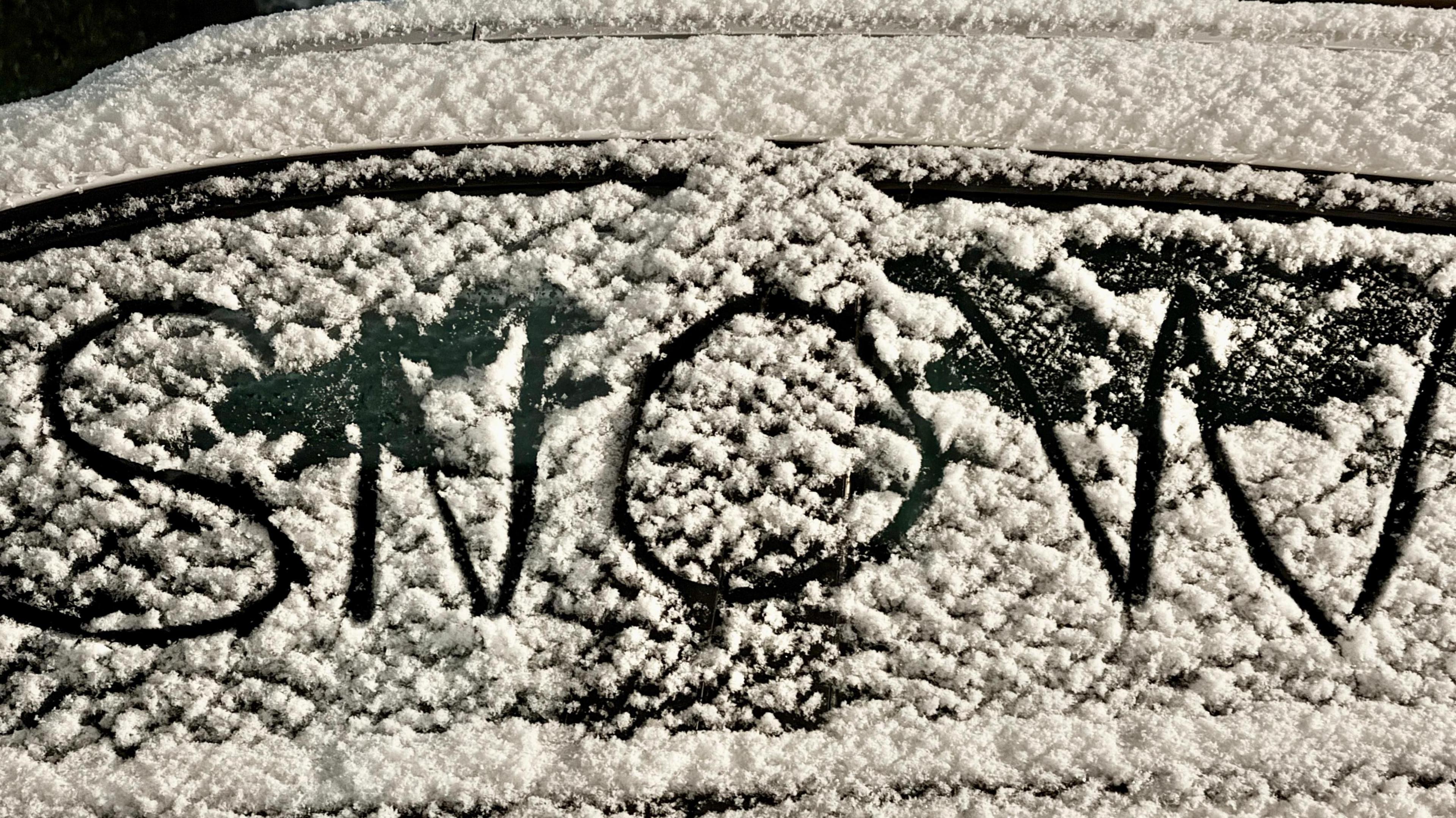 Snow-covered car windscreen with the word snow written on it.