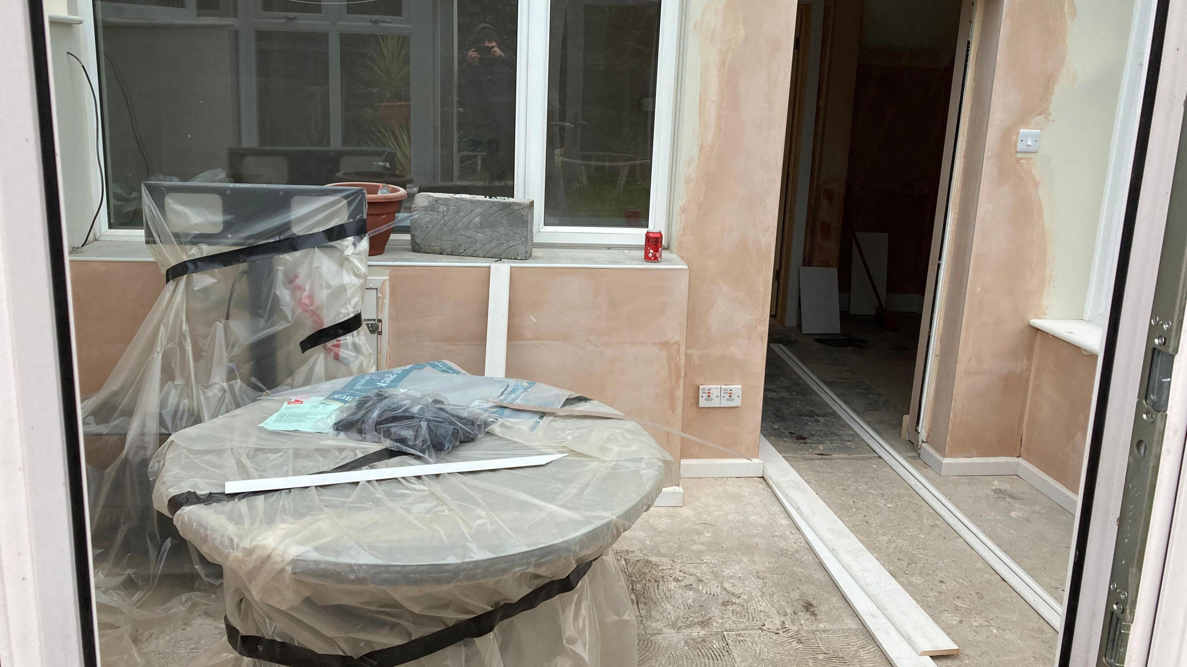 The conservatory area in Sid Traynor's home which shows freshly plastered walls, bare flooring and furniture covered with plastic sheeting