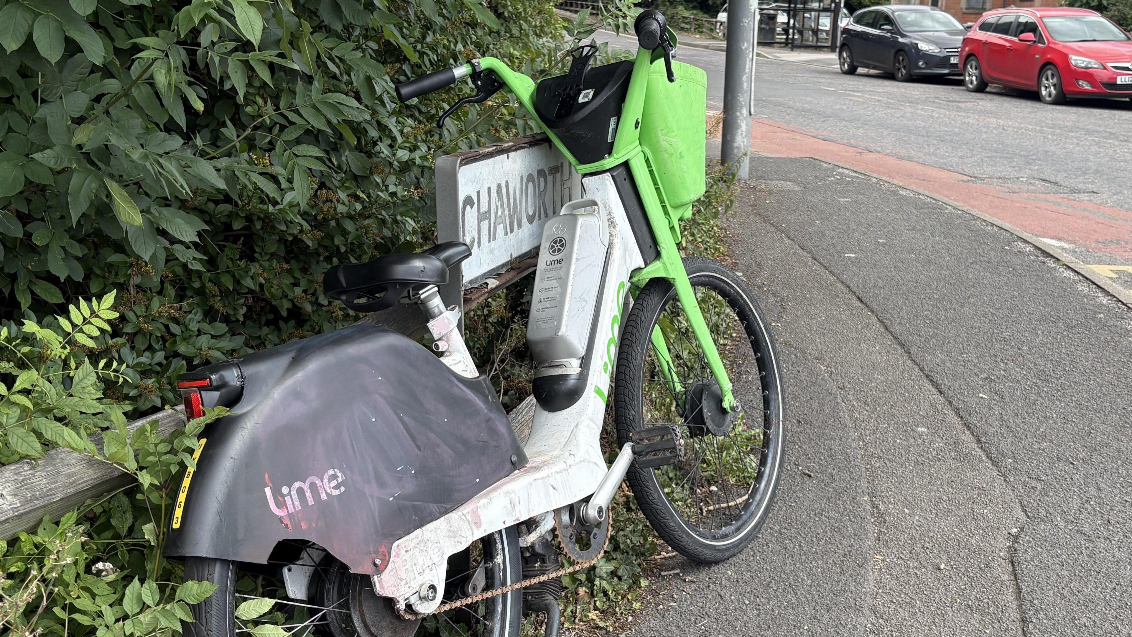 A battered looking lime bike leaning against a street sign on the side of a road.