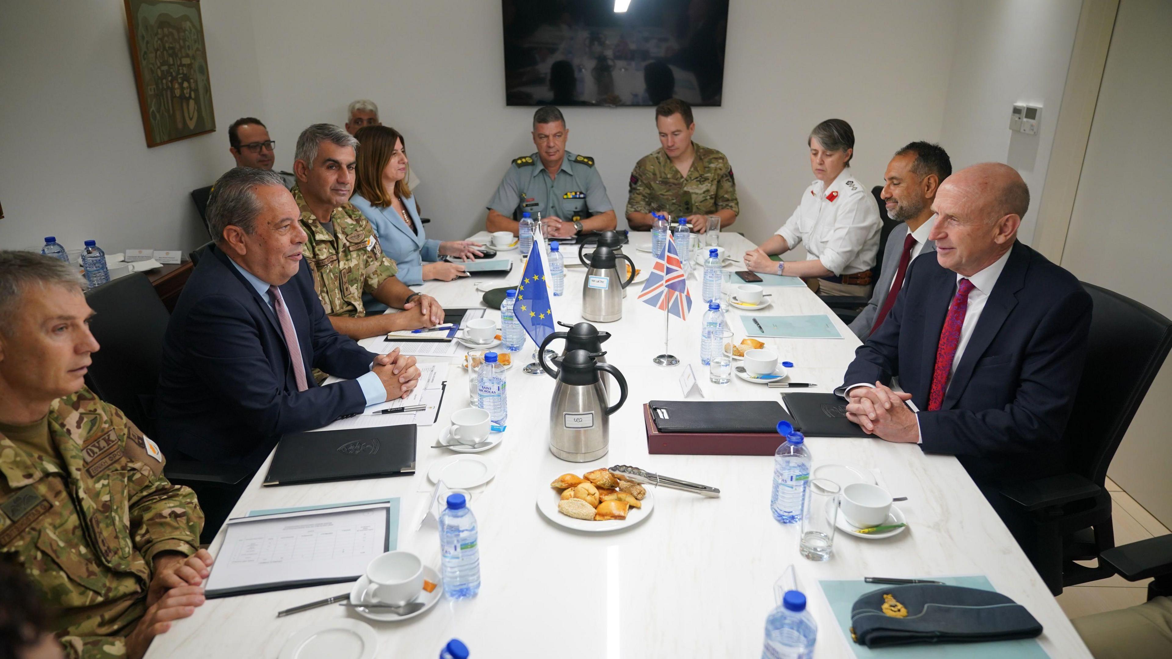 Vasilis Palmas and John Healey sitting around a white table with various military generals