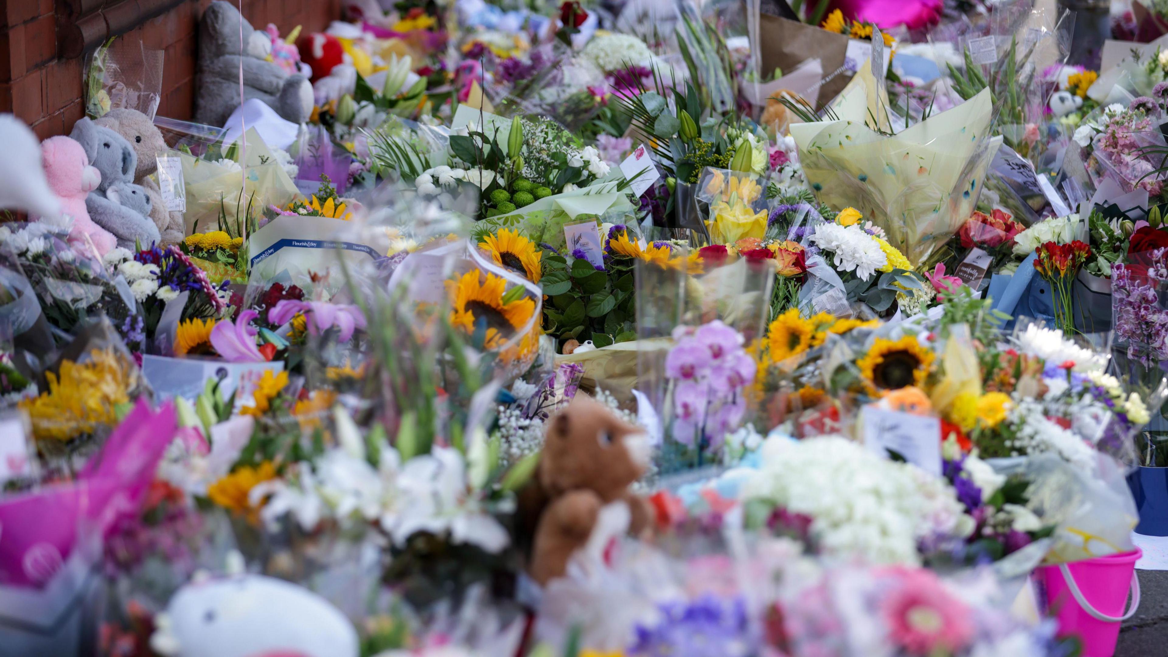 A sea of multi-coloured floral tributes and cuddly toys lie on a street close to the scene of a knife attack