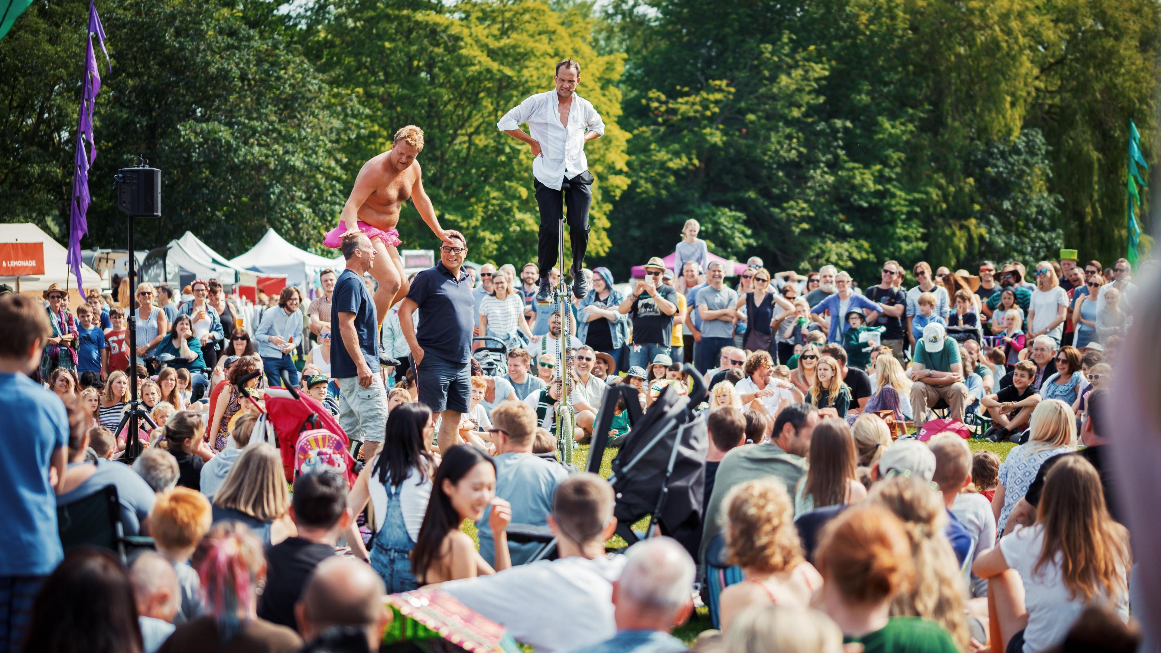 Four men performing in front of crowds of people and two of the men are on unicycles