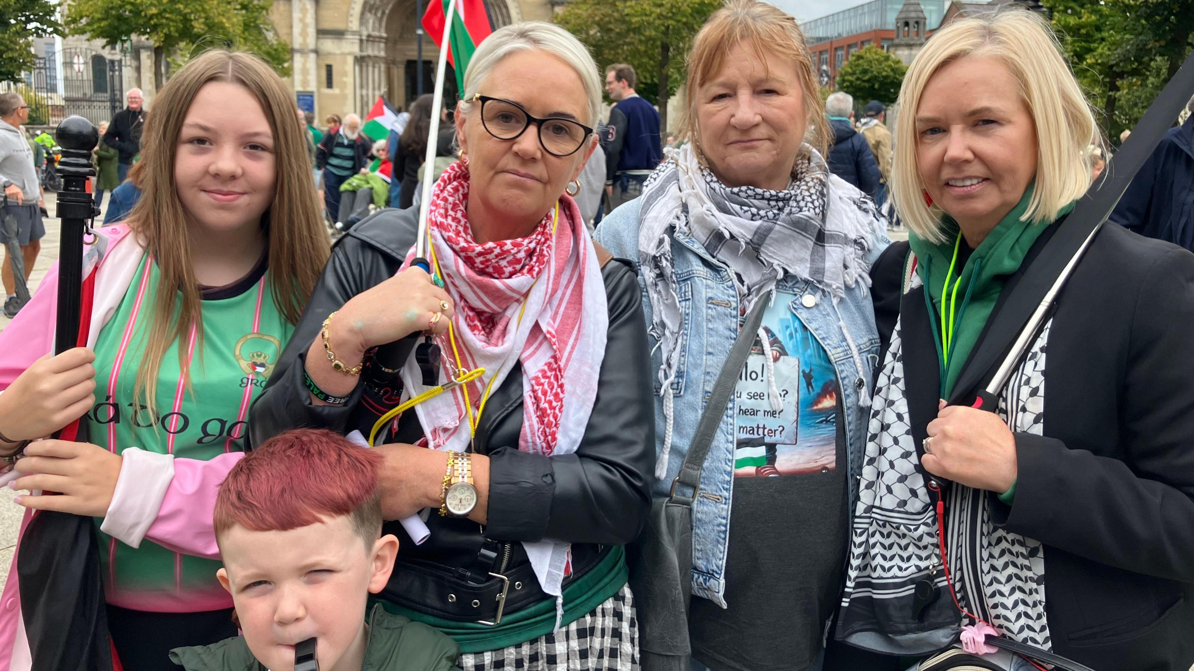 Mary Kelly and family members at the Belfast protest on Saturday. Three women with blonde hair, a young girl with long blond hair and a young boy with short red hair stand in front of St Anne's Cathedral. The woman in the middle is carrying a Palestinian flag. The boy is blowing into a whistle.
