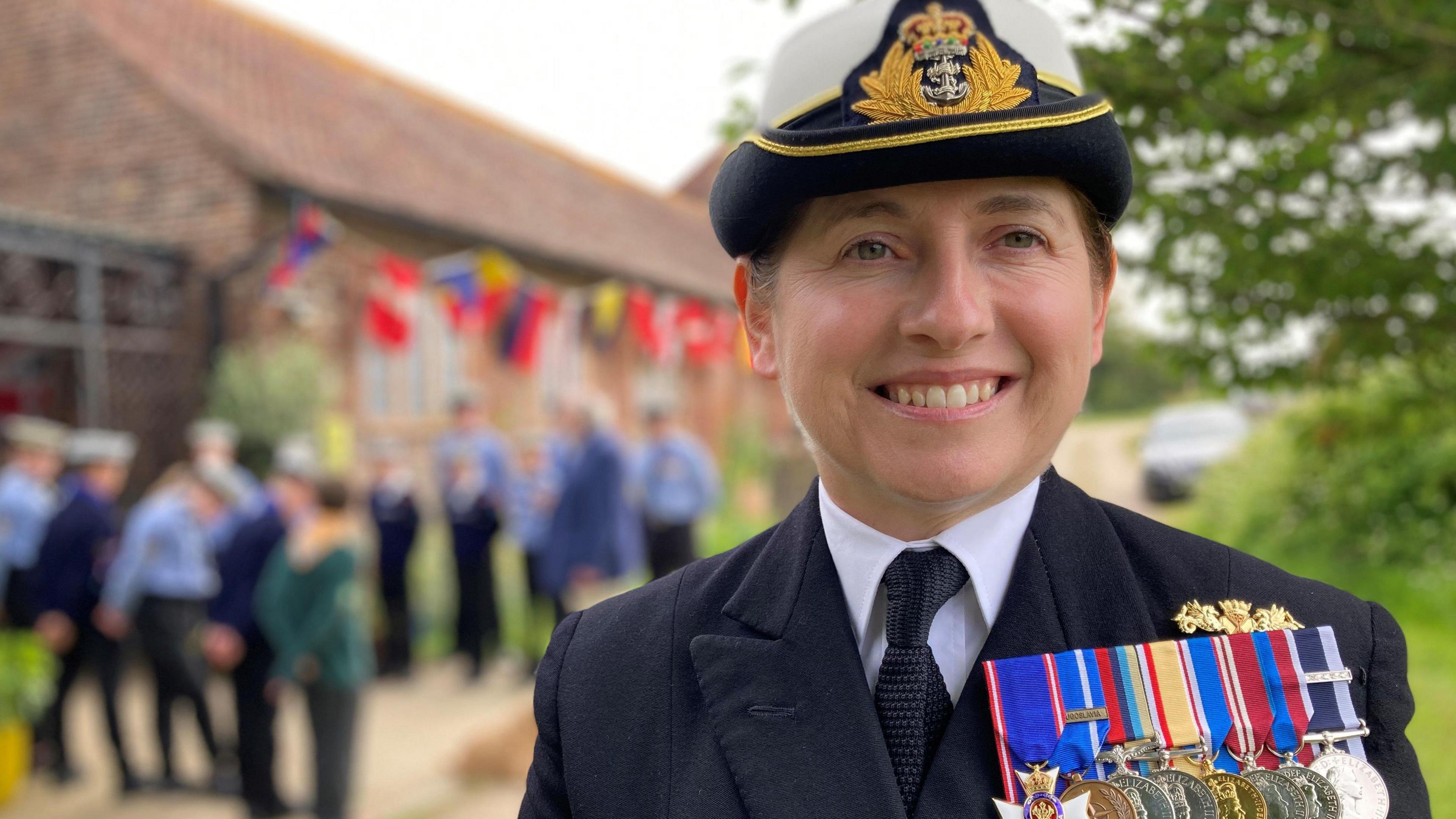 Commodore Catherine Jordan, a white middle aged woman wearing a Royal Navy uniform and eight medals on her left smiling at the camera