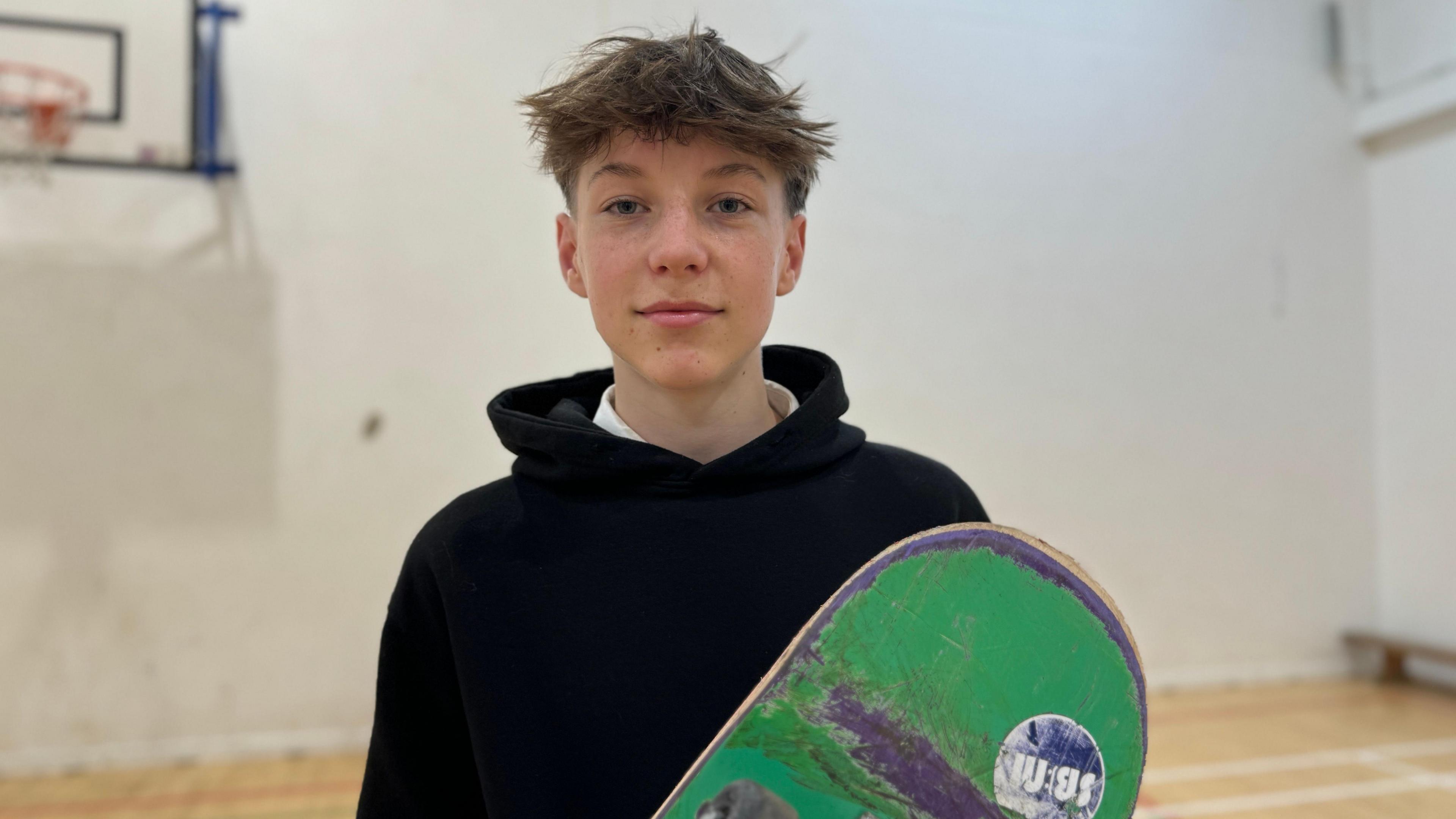 Theo (16) smiles with his skateboard.