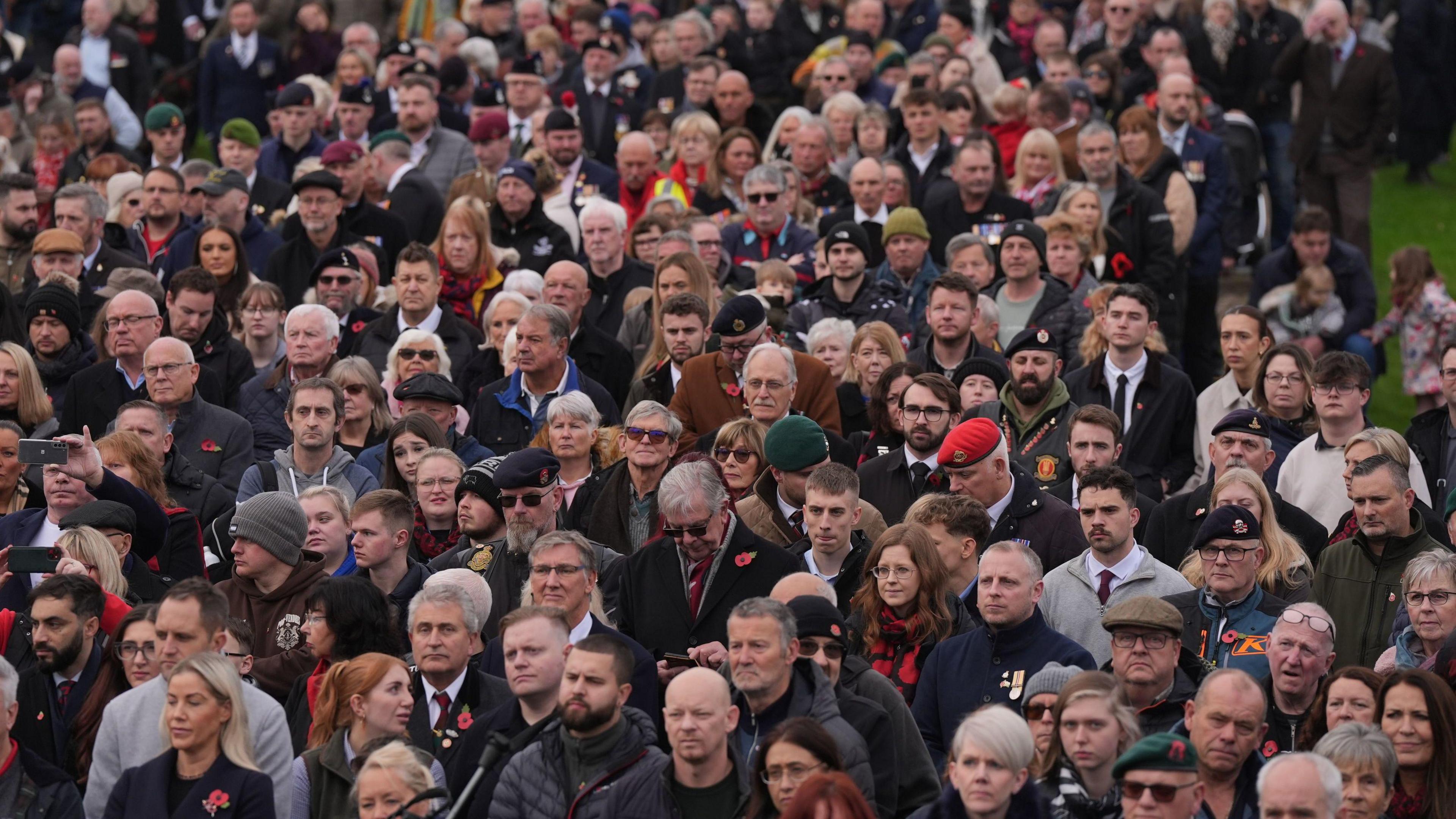 A crowd of people wearing coats with red poppies on their chests