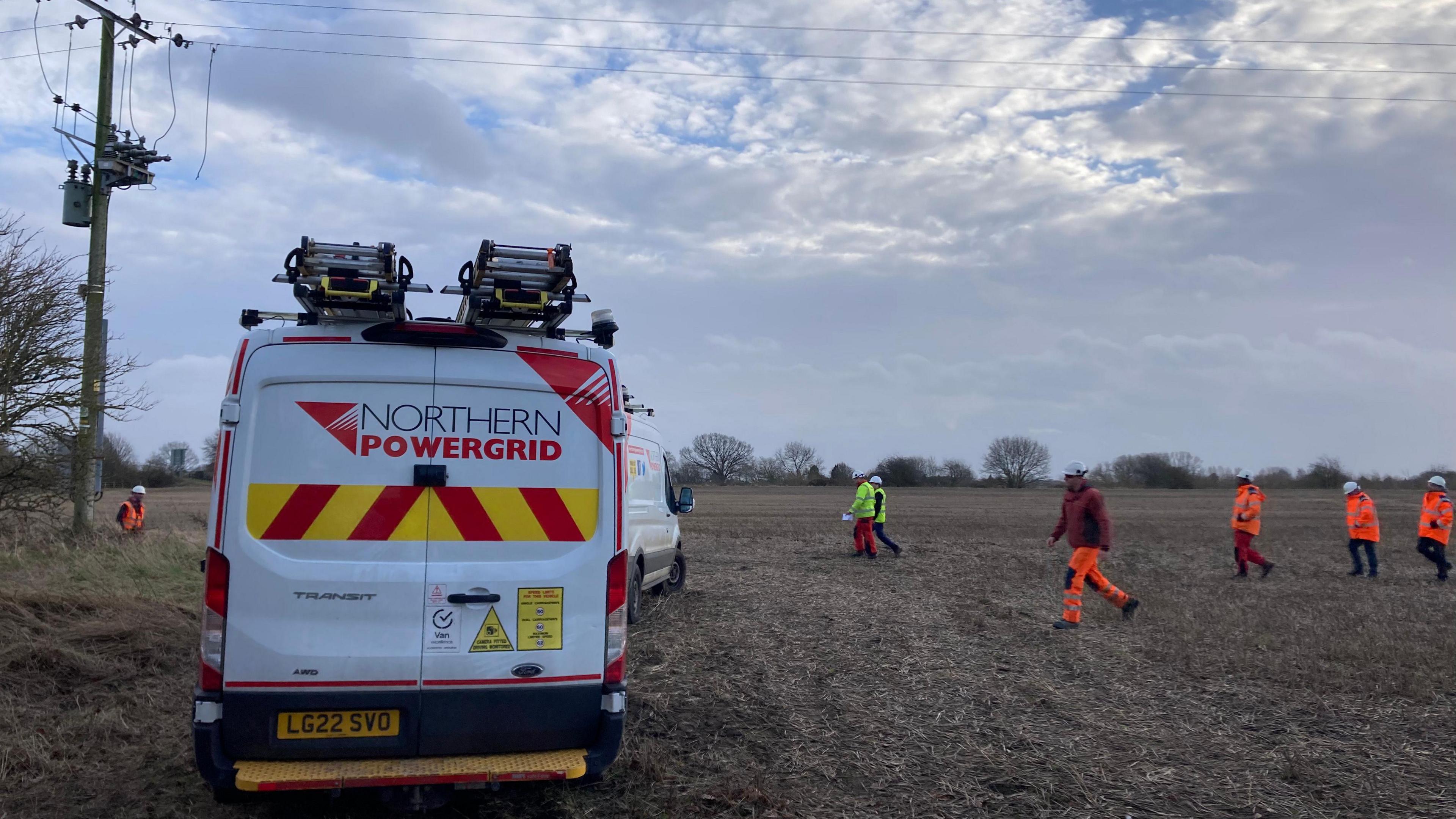 A parked van with the words "Northern Powergrid" on the back doors. A group of men in hi-vis clothing are walking towards the vehicle.