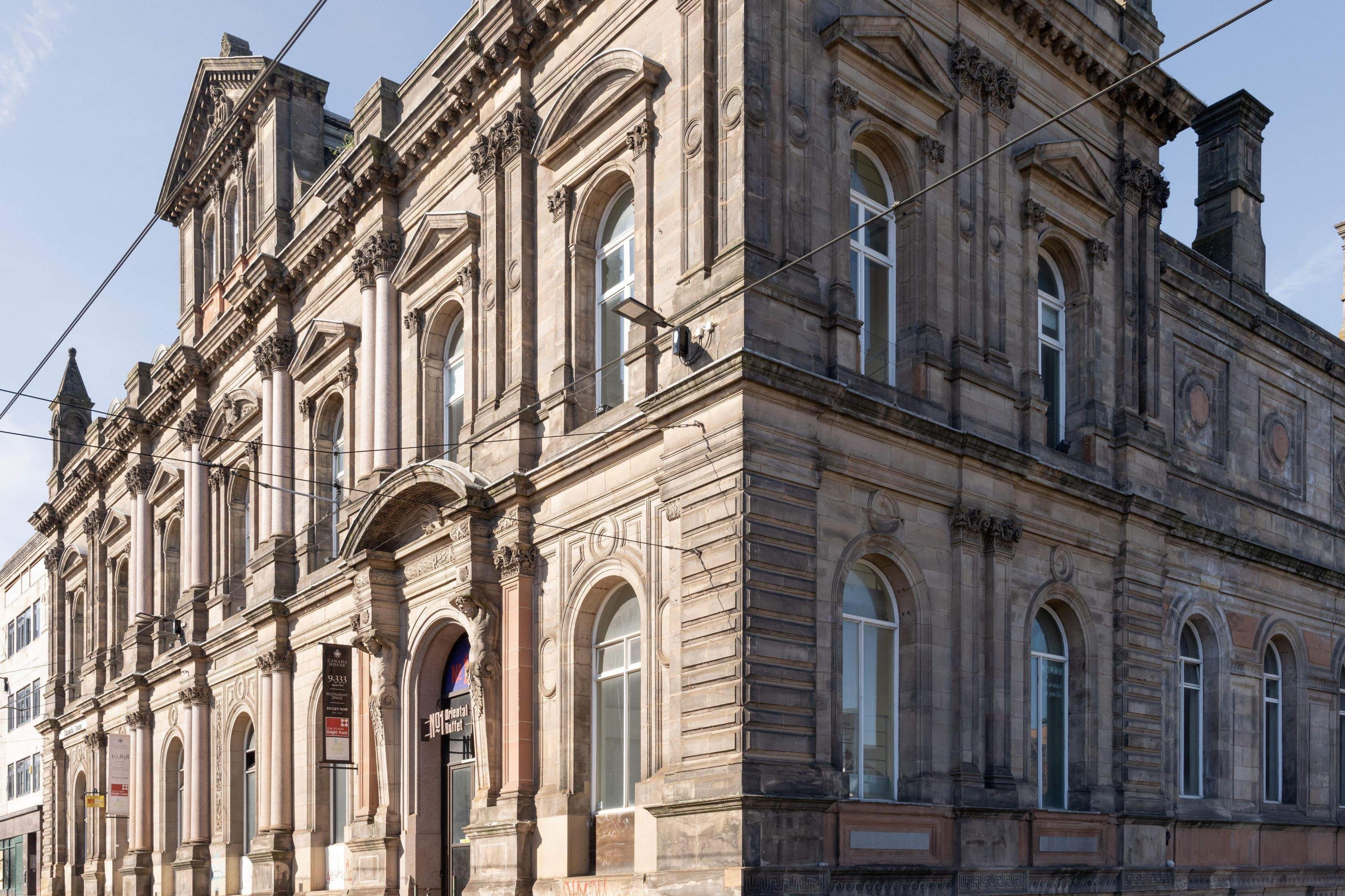 Canada House is a Victorian stone building, five storeys high with ornate windows, brickwork and two statues overlooking the front entrance