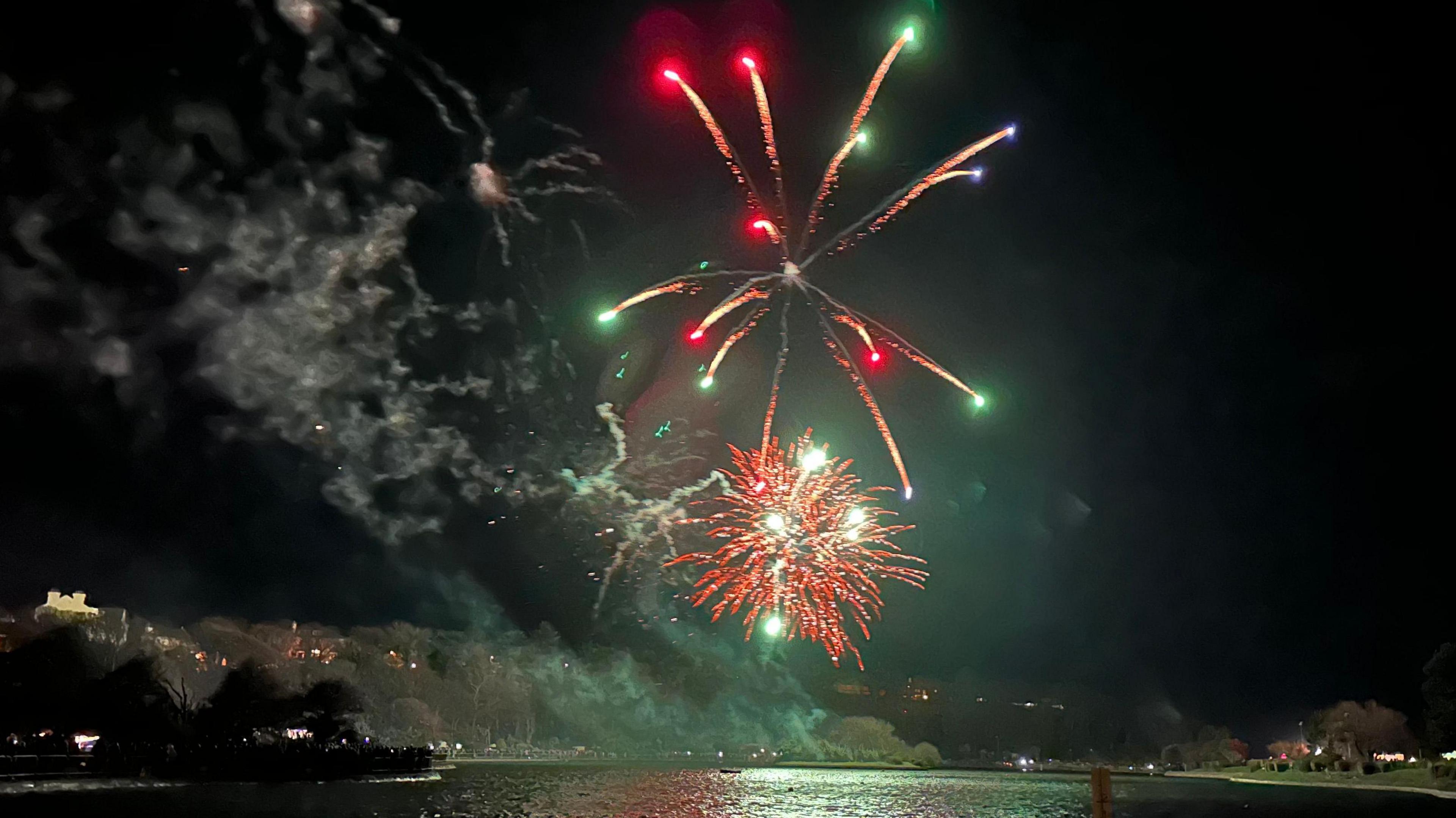 A green and red firework exploding over the Mooragh Park lake at night.