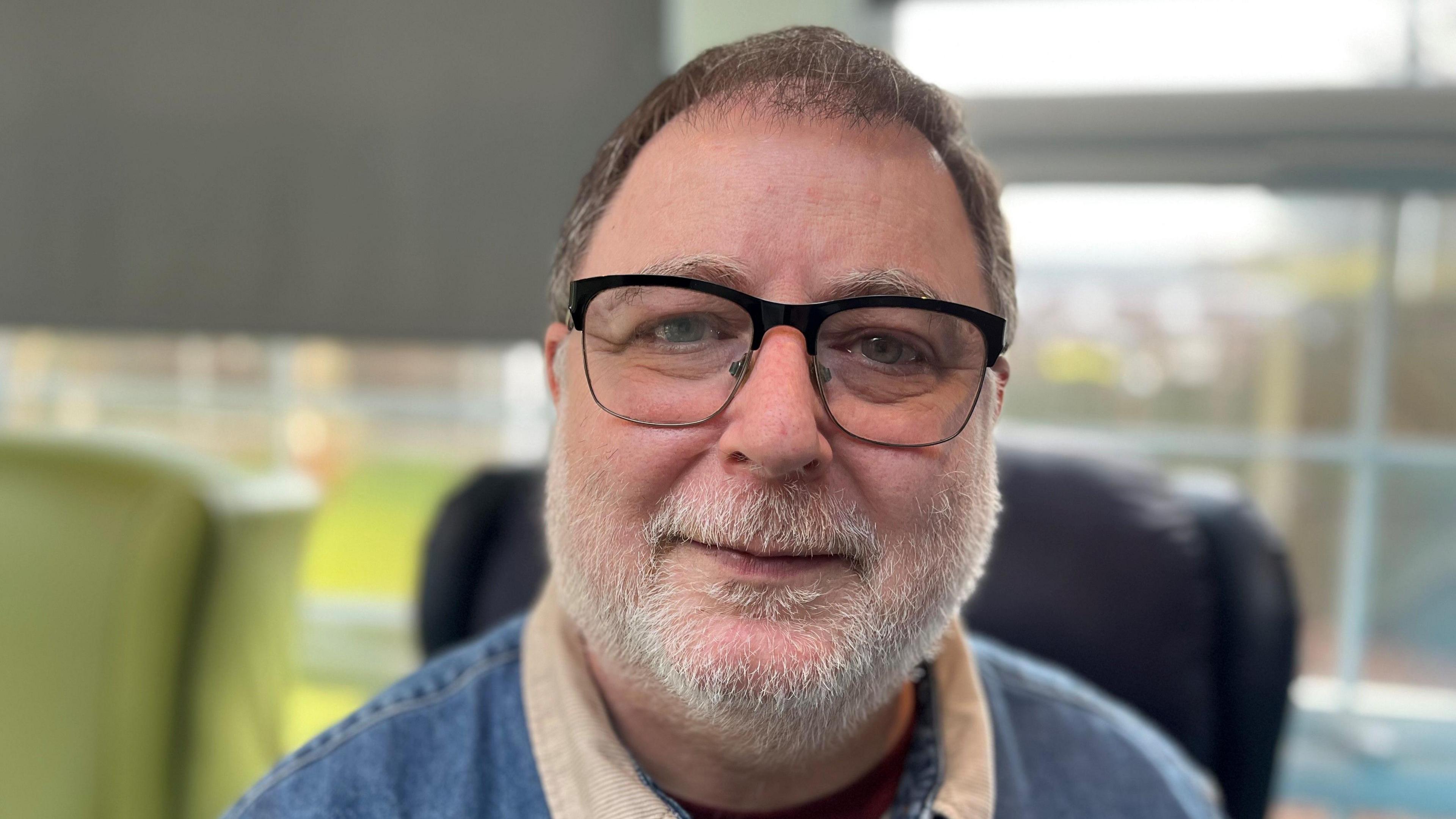 Danny, a man in his 50s, with glasses and a grey beard, wearing a denim shirt