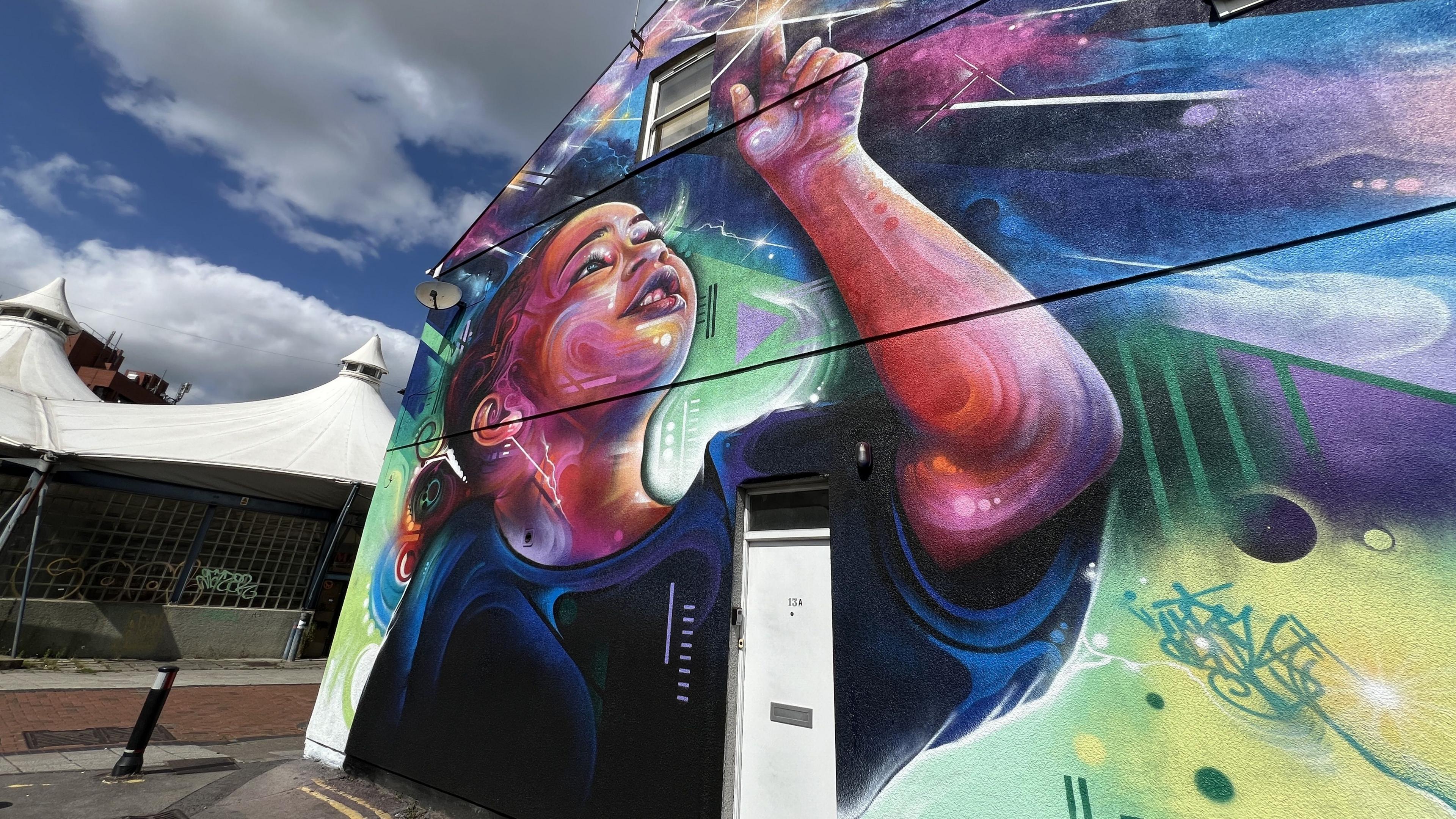 A colourful mural painted onto the front of a house - the mural features a child reaching up to touch a bright light