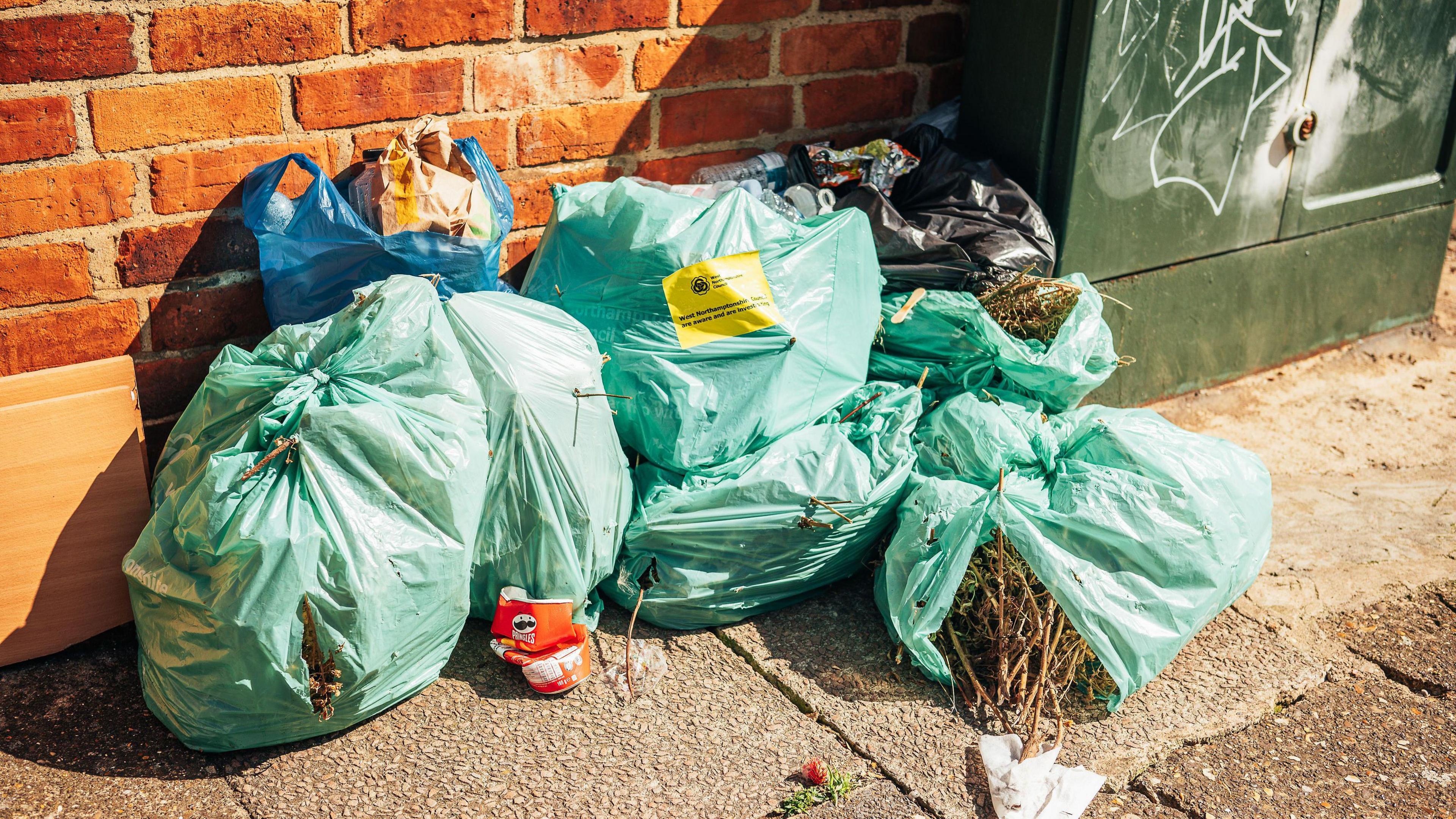 Six bags of rubbish left by a brick wall